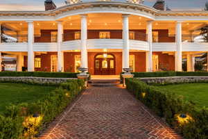 Exterior entry at dusk with brick siding, mansard roof, and a yard