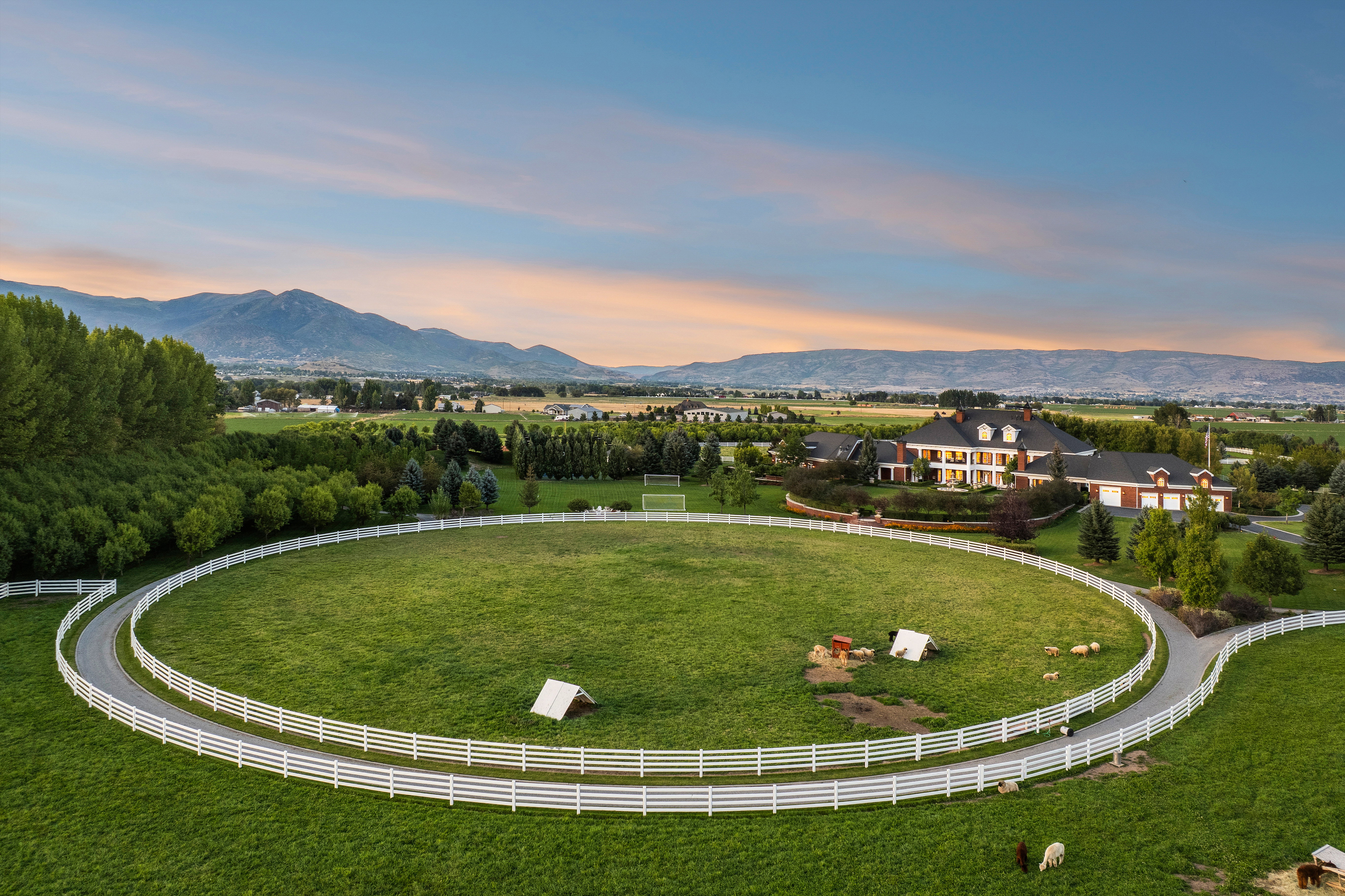 Expansive grounds featuring a circular fenced pasture with a paved drive, surrounded by mature trees