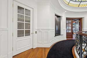 Hall featuring wood finished floors, ornamental molding, a decorative wall, a wainscoted wall, and an upstairs landing