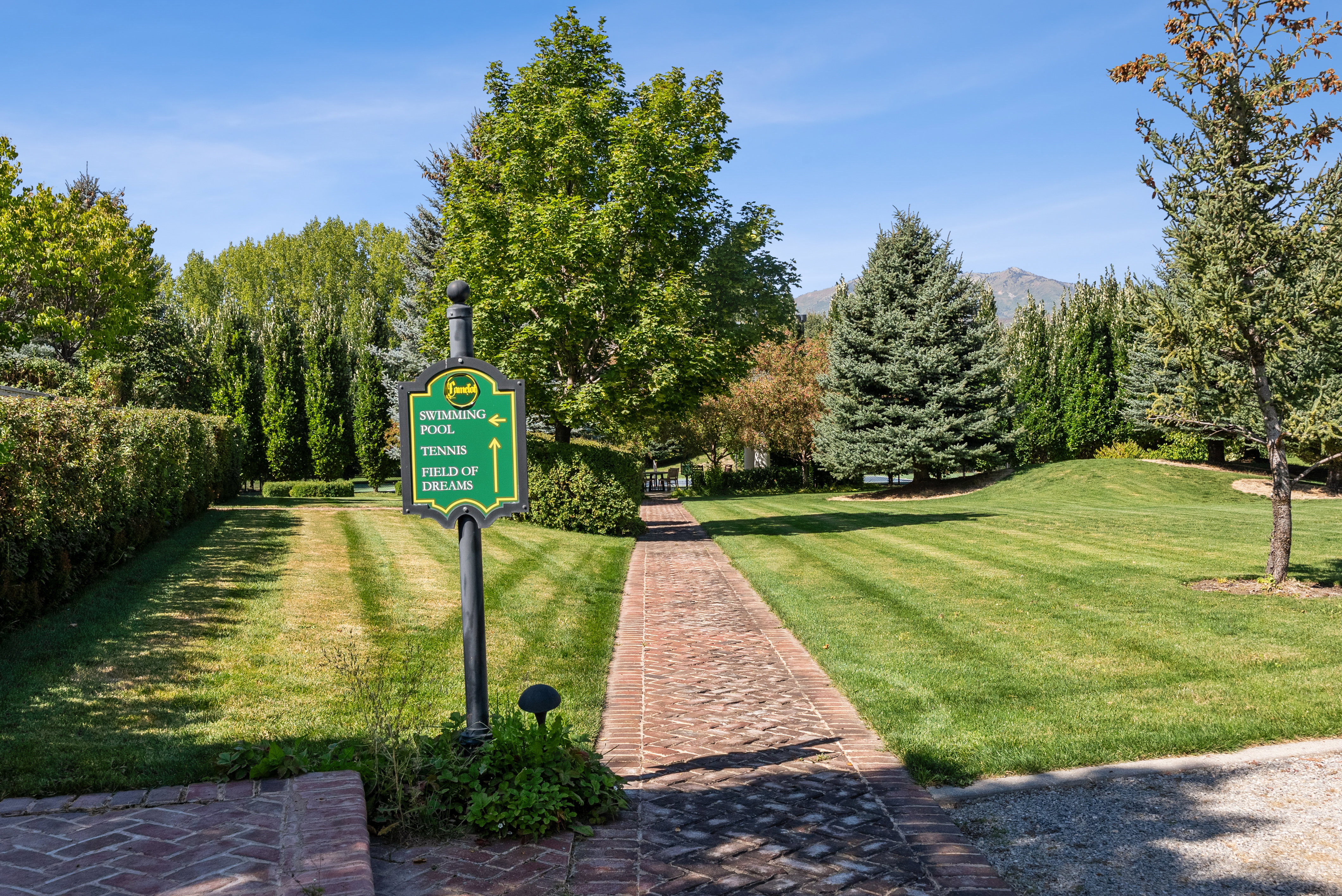 Expansive green lawn with mature trees and a brick pathway