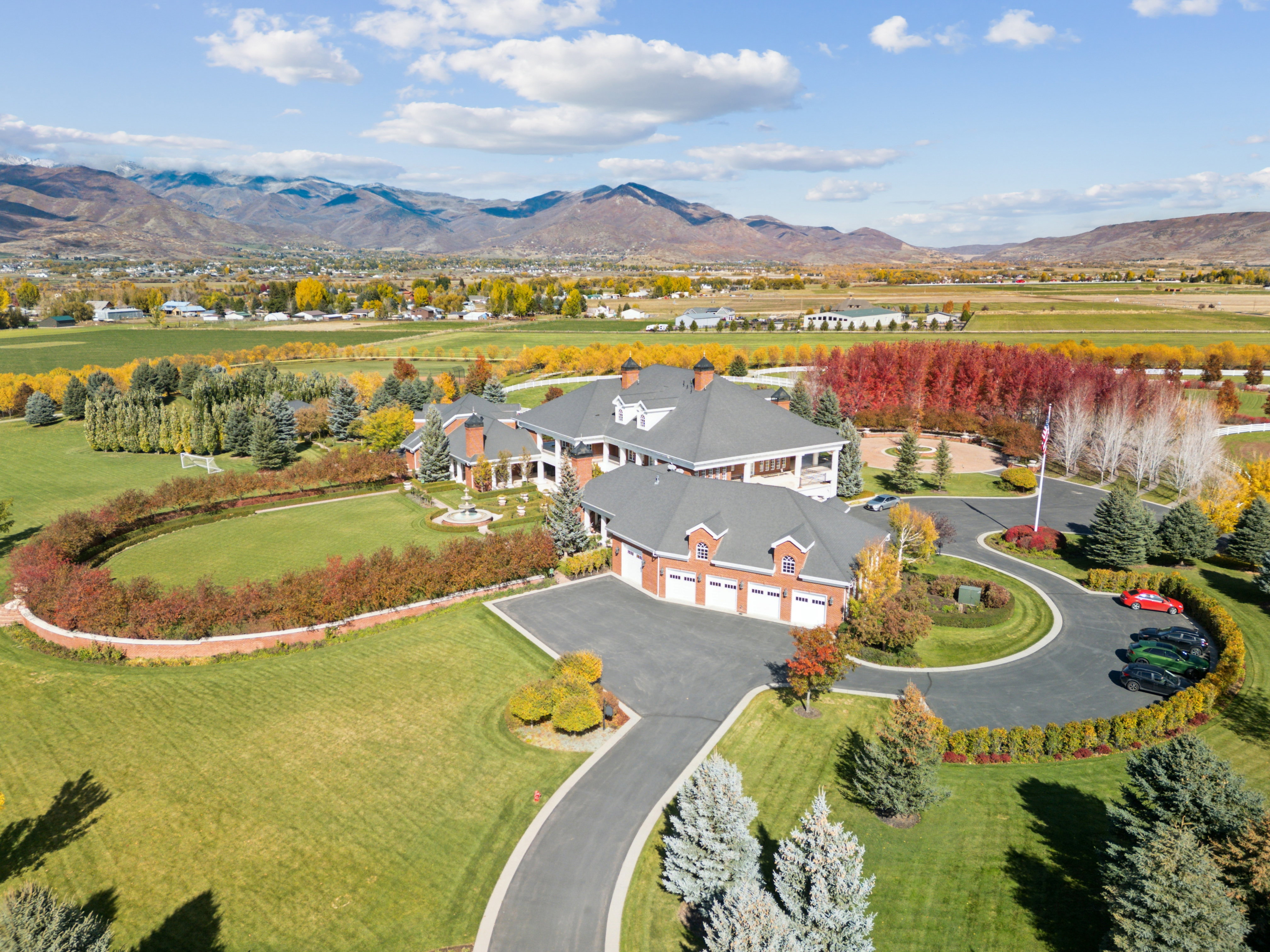 Expansive property featuring a multi-structure residence with red brick and white siding accents, a circular driveway, and a three-car garage
