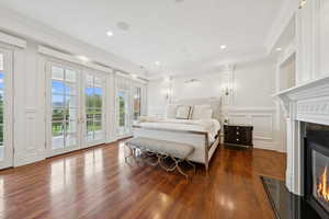 Bedroom featuring french doors, a decorative wall, a glass covered fireplace, ornamental molding, and access to outside
