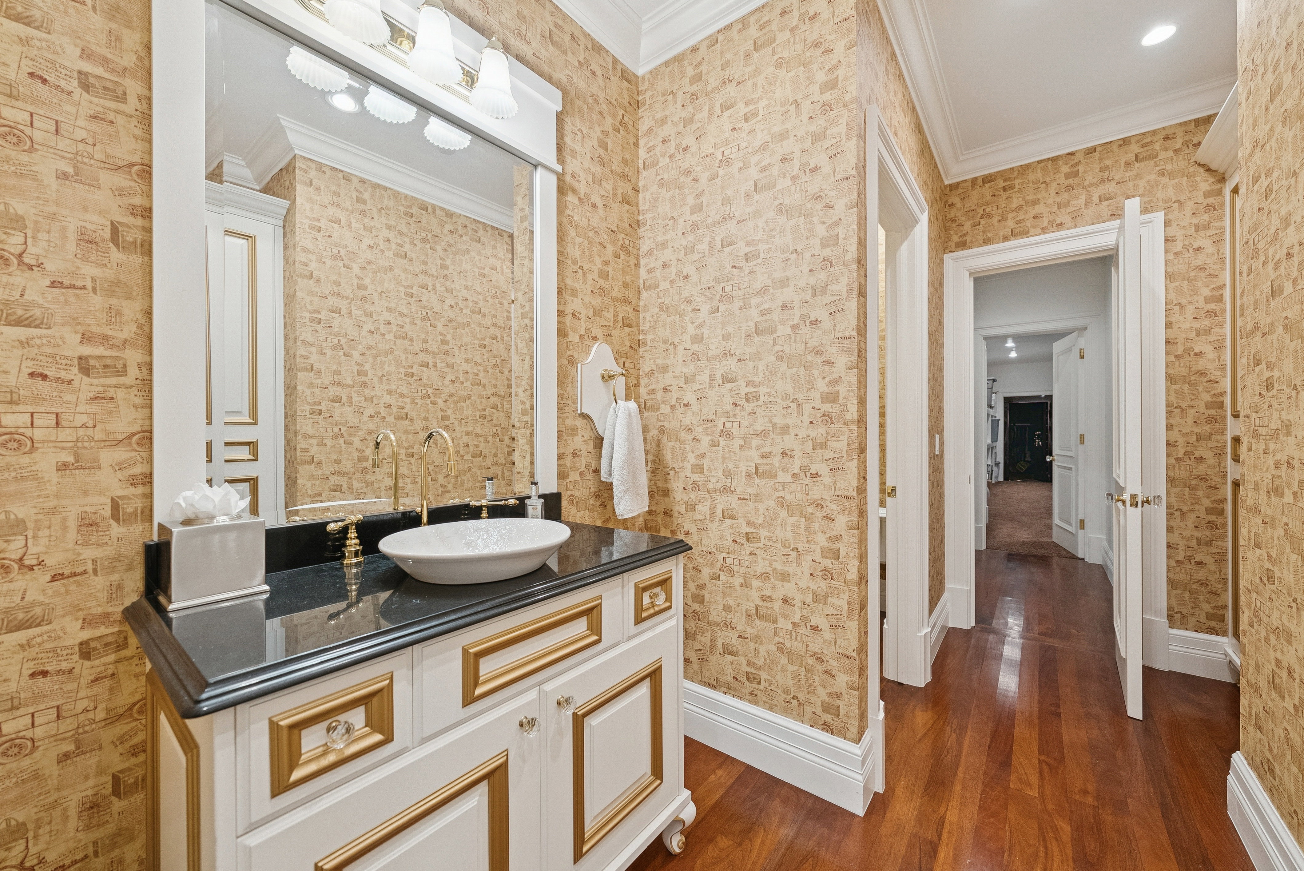 Vanity featuring a vessel sink, black countertop, gold-tone fixtures, and white cabinetry with gold trim