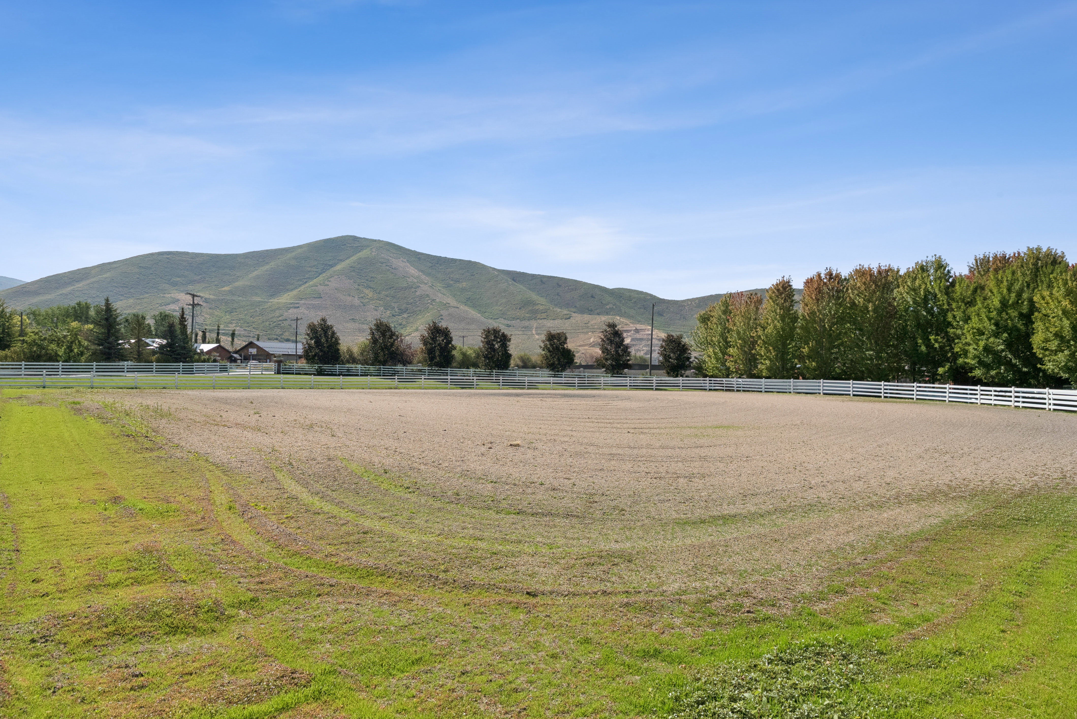 Expansive outdoor arena featuring a white perimeter fence and a groomed sand surface
