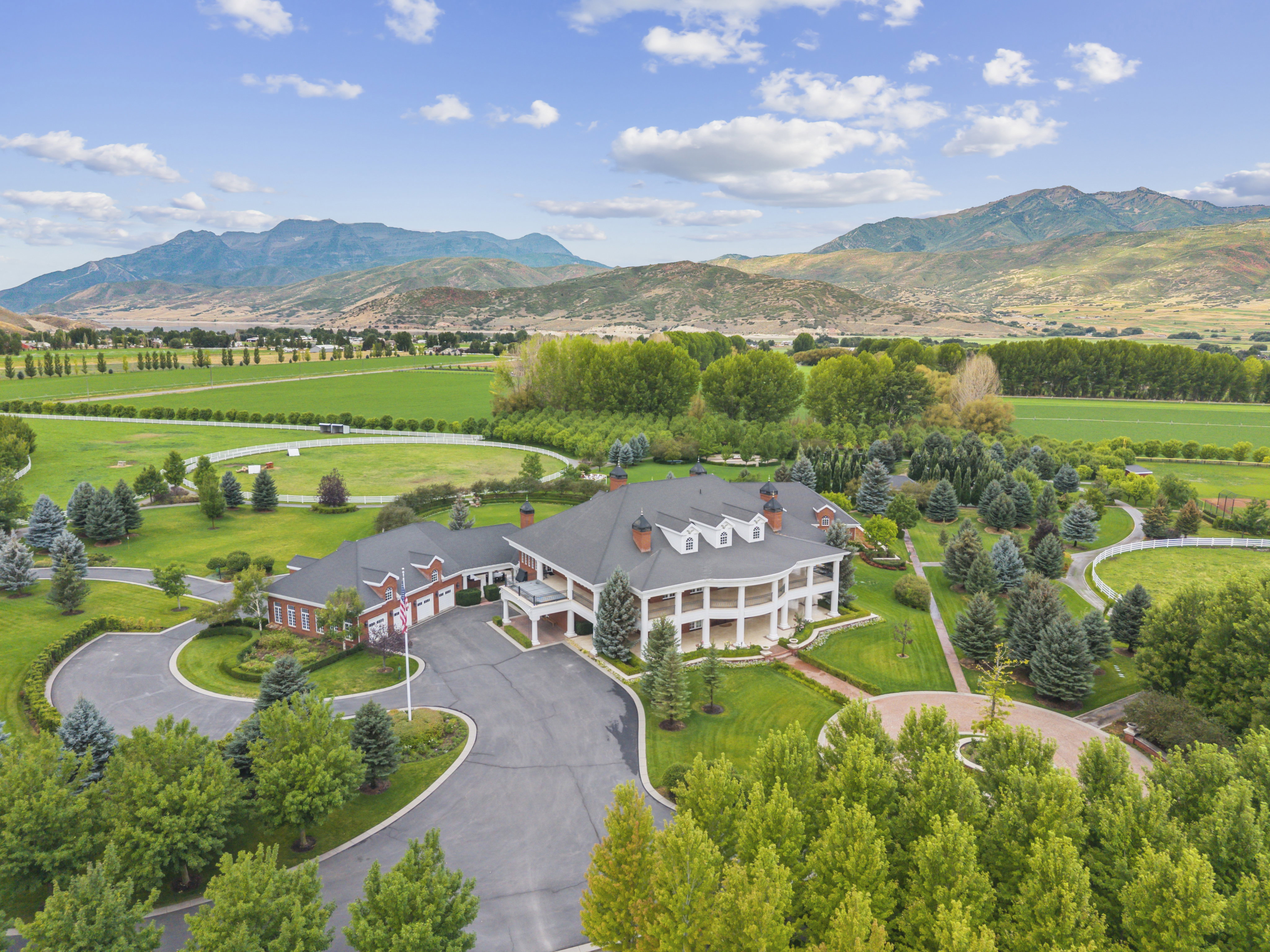 Expansive estate featuring a large brick primary residence with a multi-level porch, a substantial paved driveway, and manicured landscaping