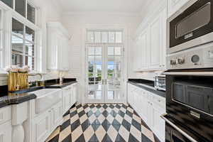 Kitchen featuring dark countertops, double oven, stainless steel microwave, white cabinetry, and french doors