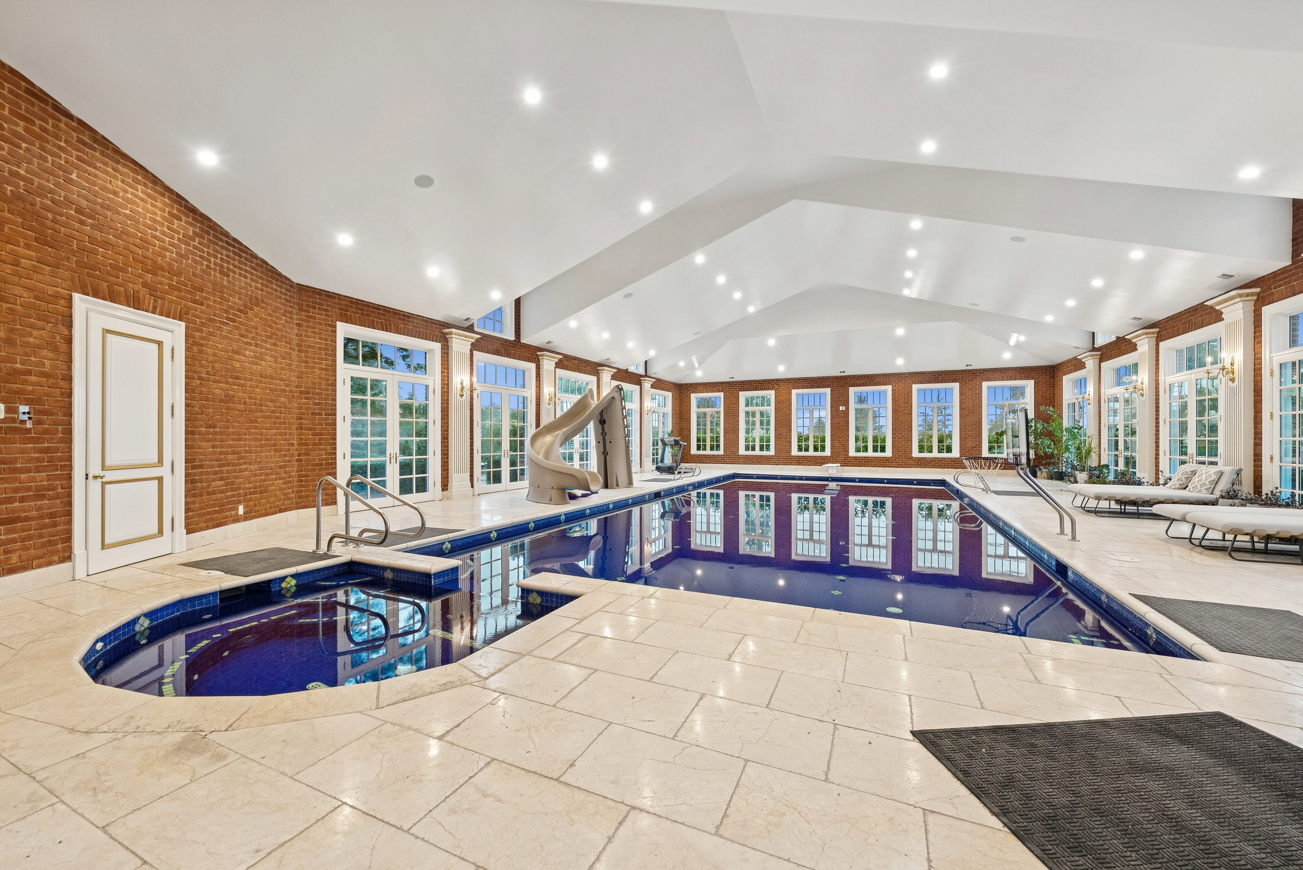 Indoor swimming pool with an integrated spa, a water slide, and a vaulted ceiling with recessed lighting
