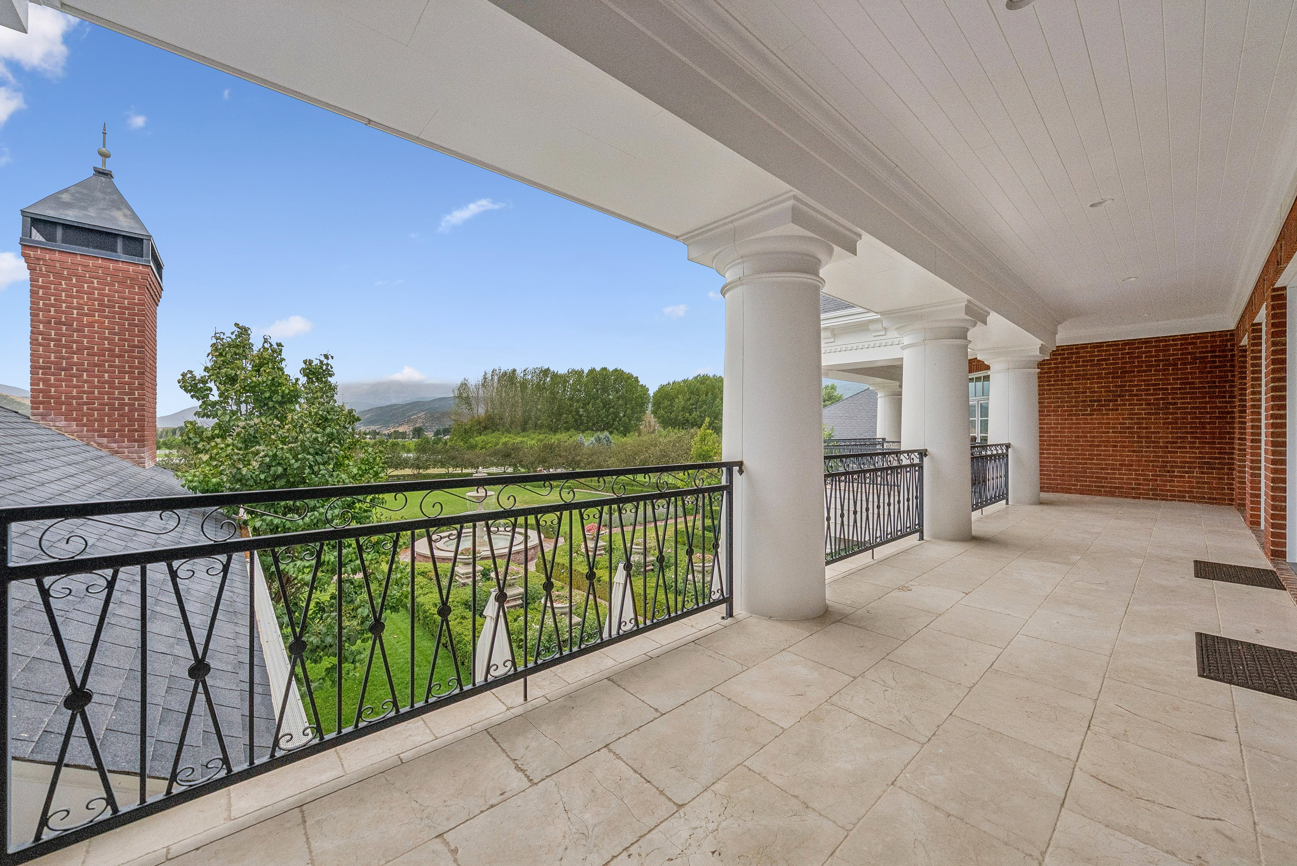 Expansive covered patio featuring large format tile flooring, decorative wrought iron railing, and substantial architectural columns