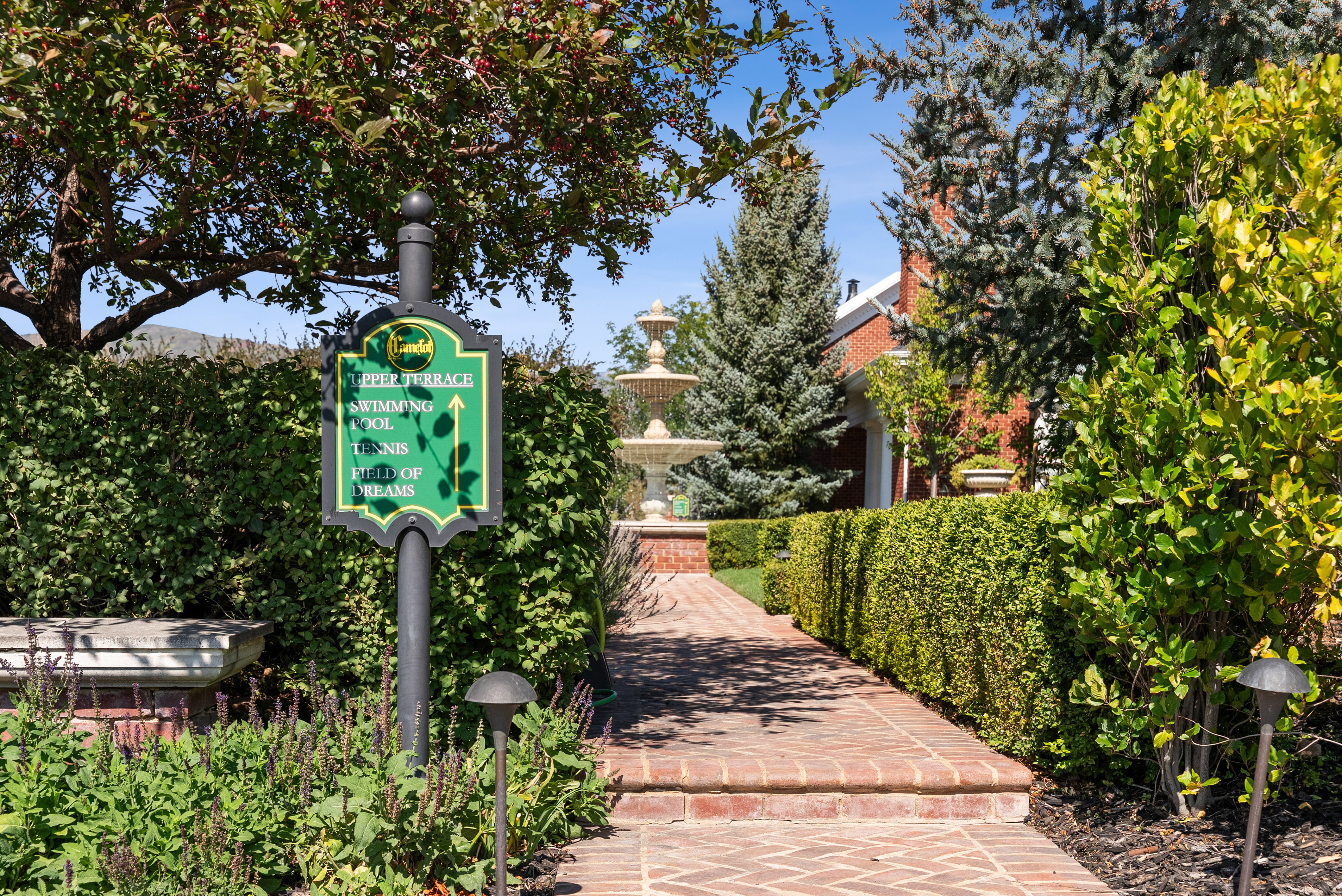 Brick pathway bordered by manicured hedges leading to a multi-tiered fountain