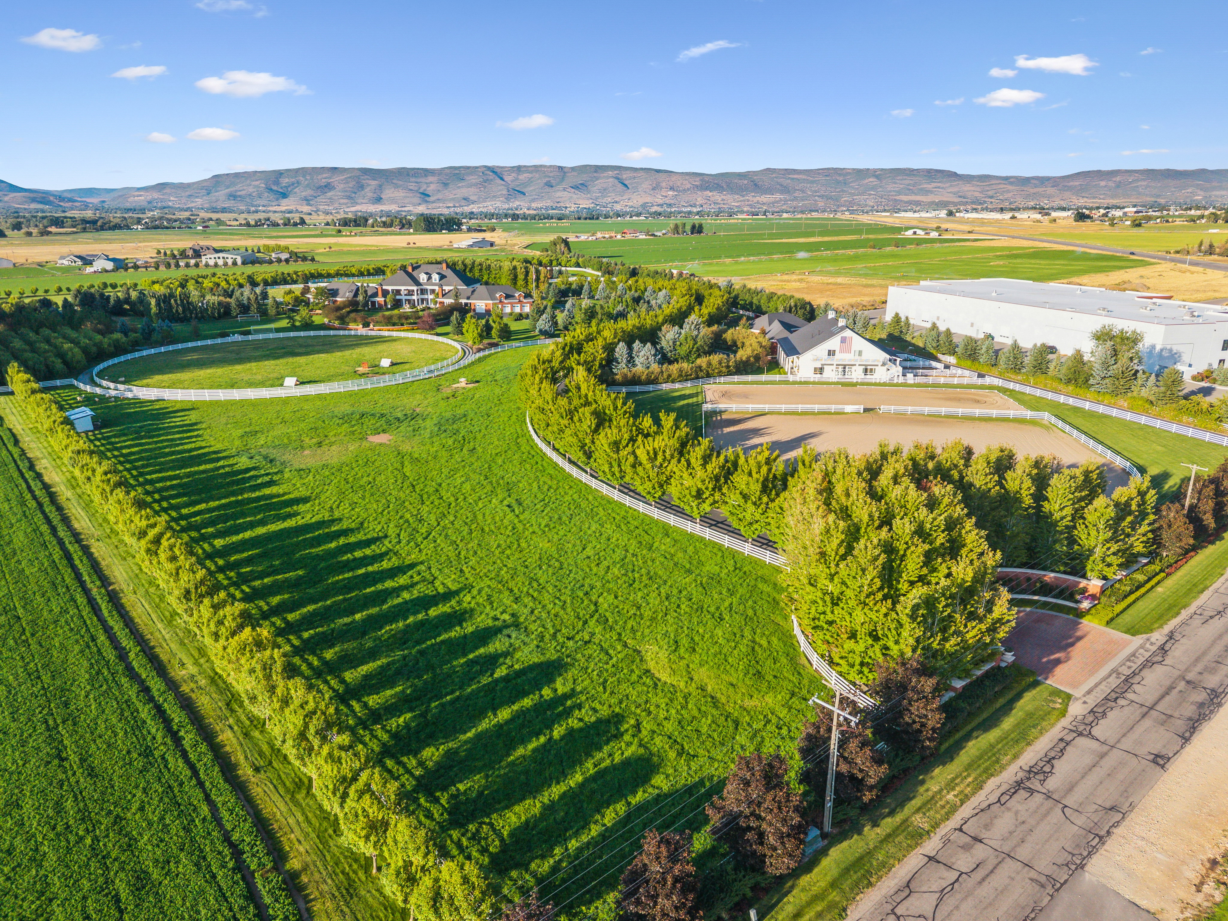 Expansive green acreage featuring a round riding arena, additional rectangular riding arena, and mature trees providing natural screening