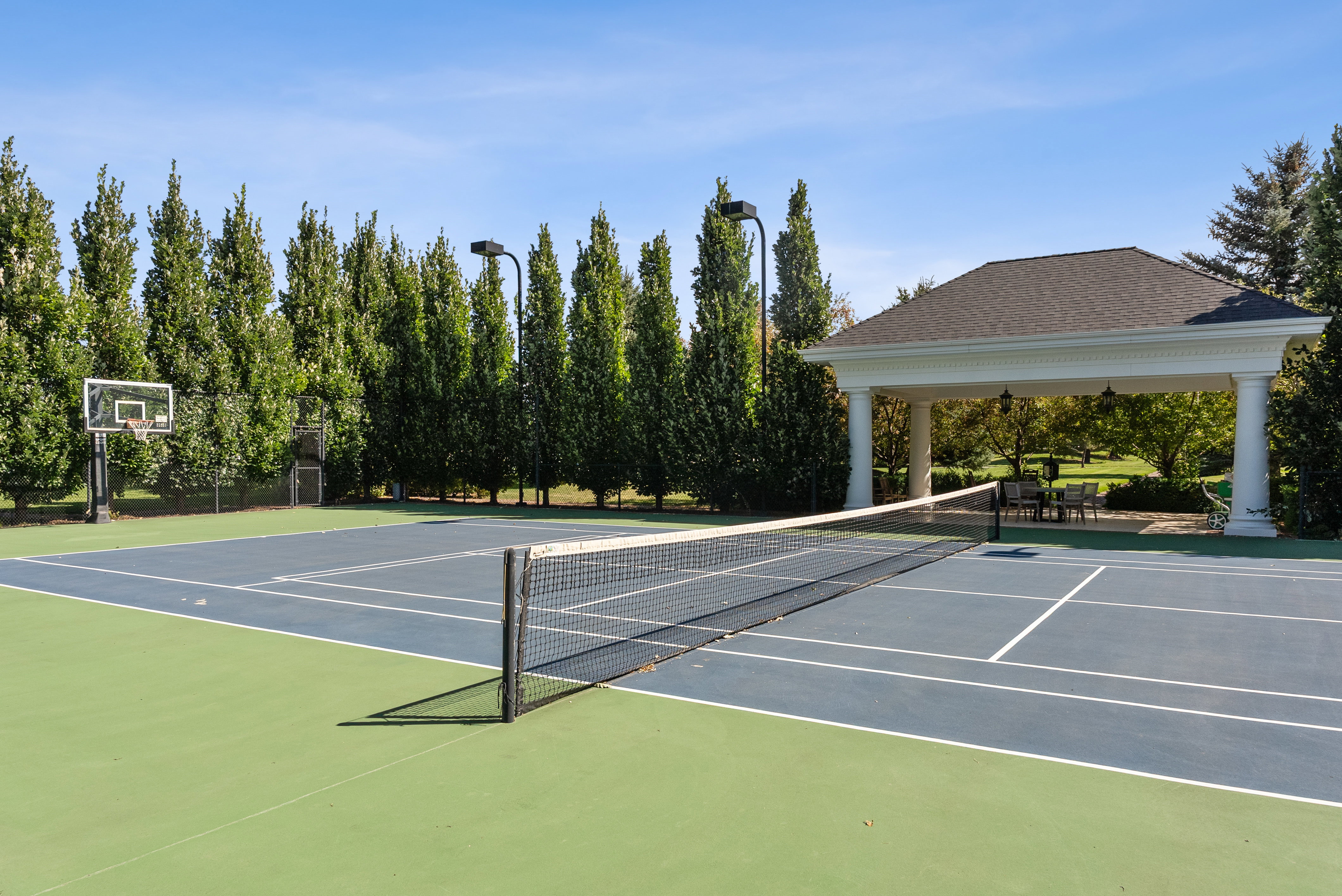 Multi-sport court featuring a tennis net, green and blue playing surfaces, and a basketball hoop