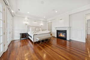 Bedroom featuring a decorative wall, ornamental molding, a premium fireplace, dark wood finished floors, and recessed lighting