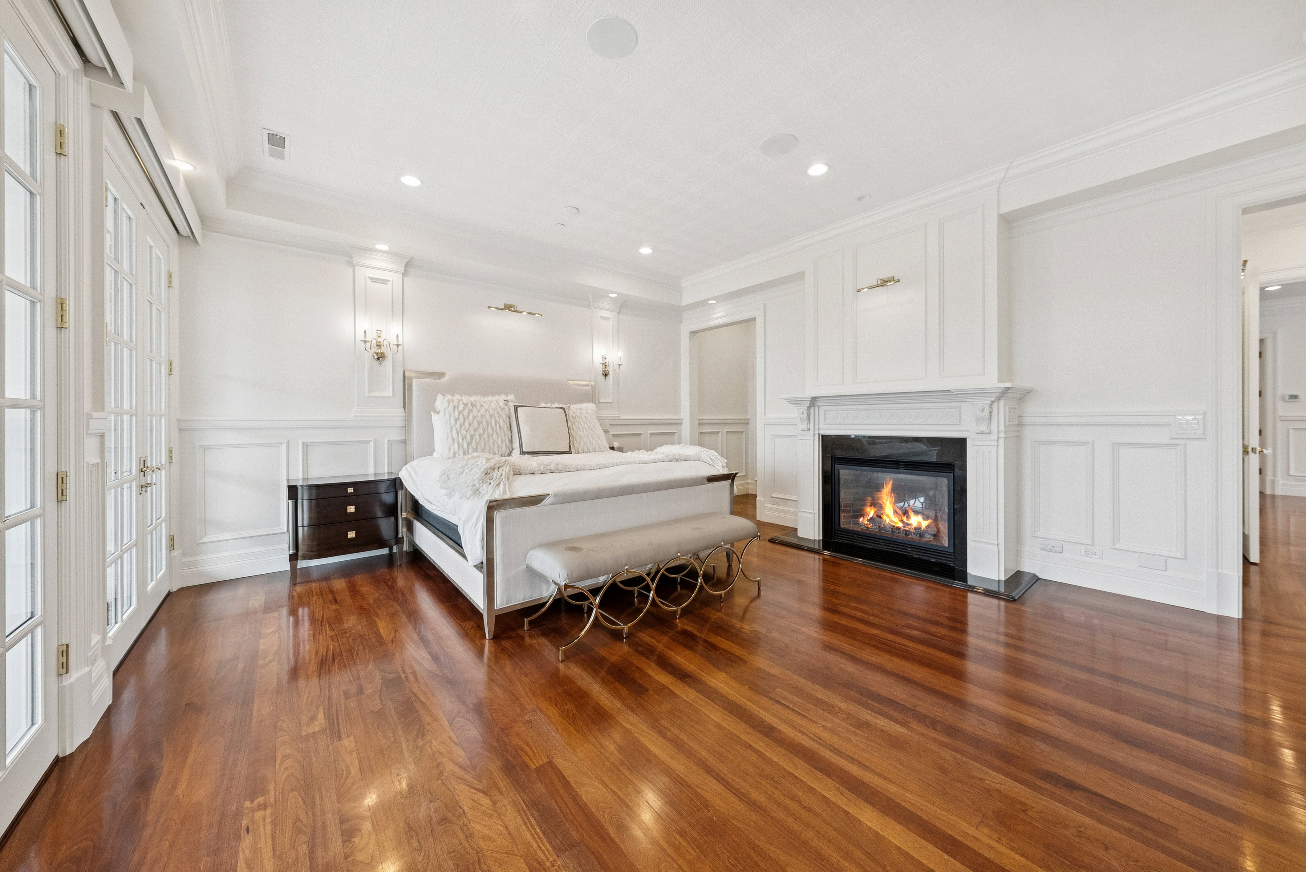 Spacious room featuring rich wood-finish flooring, white paneling, and a classic fireplace with a black surround