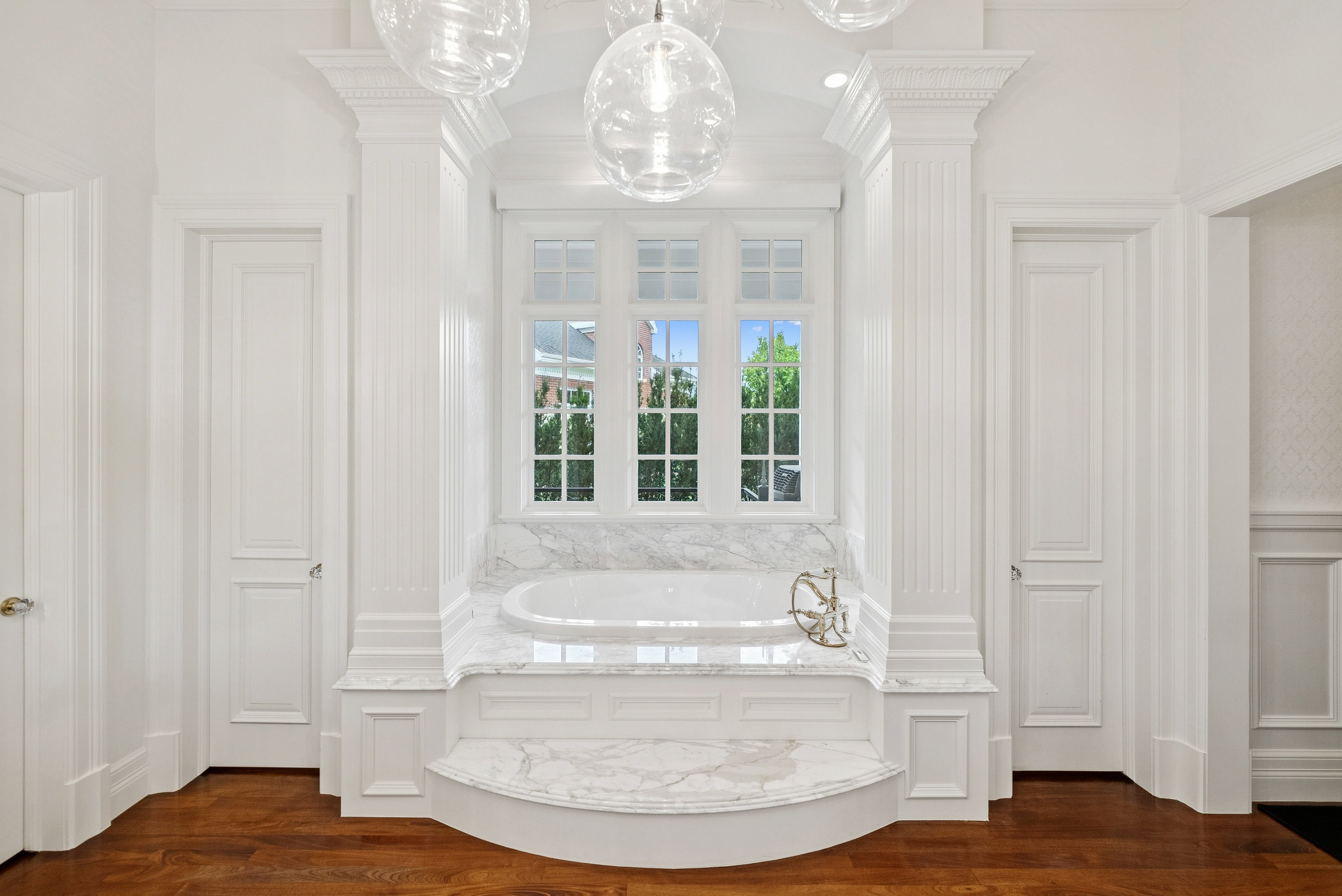 Soaking tub set within a marble surround, flanked by fluted columns and paneled walls