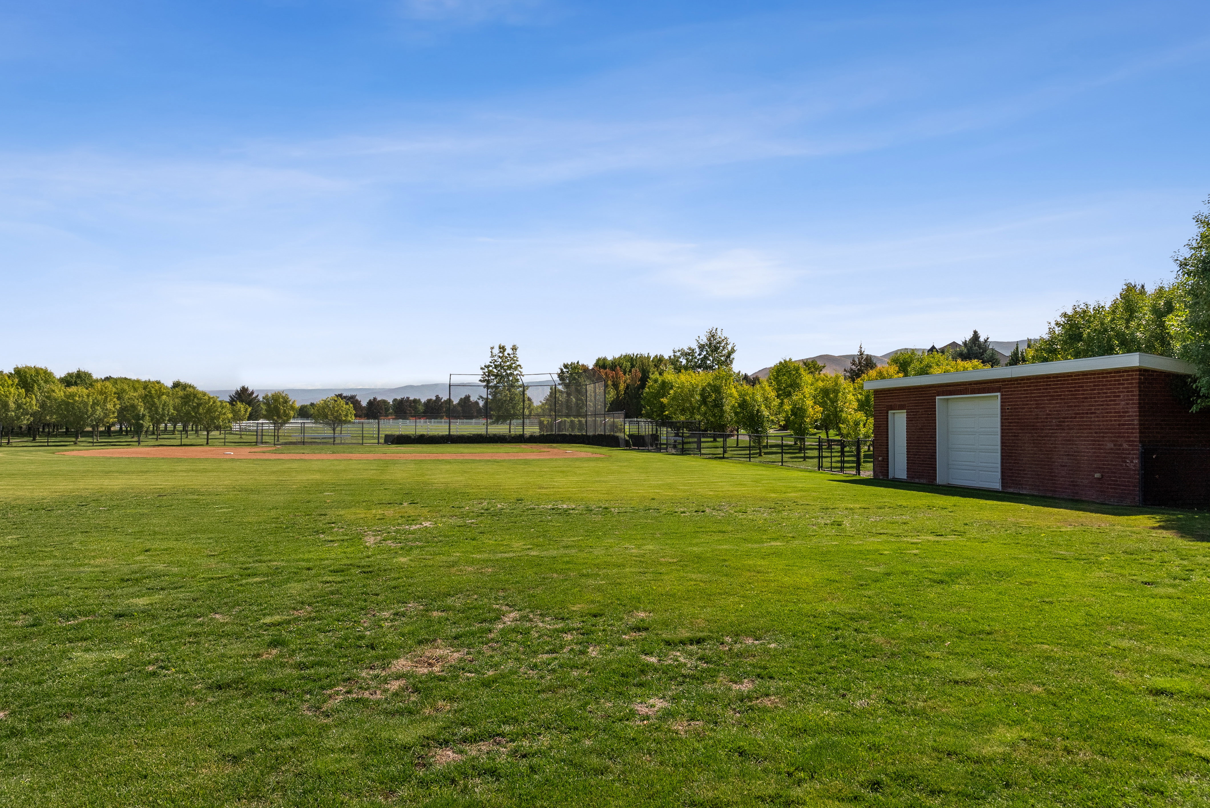 Expansive green space featuring a red brick utility building with a roll-up garage door and a side entry door