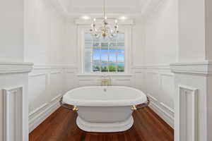 Full bathroom with a freestanding bath, dark wood-style floors, a decorative wall, a raised ceiling, and ornamental molding