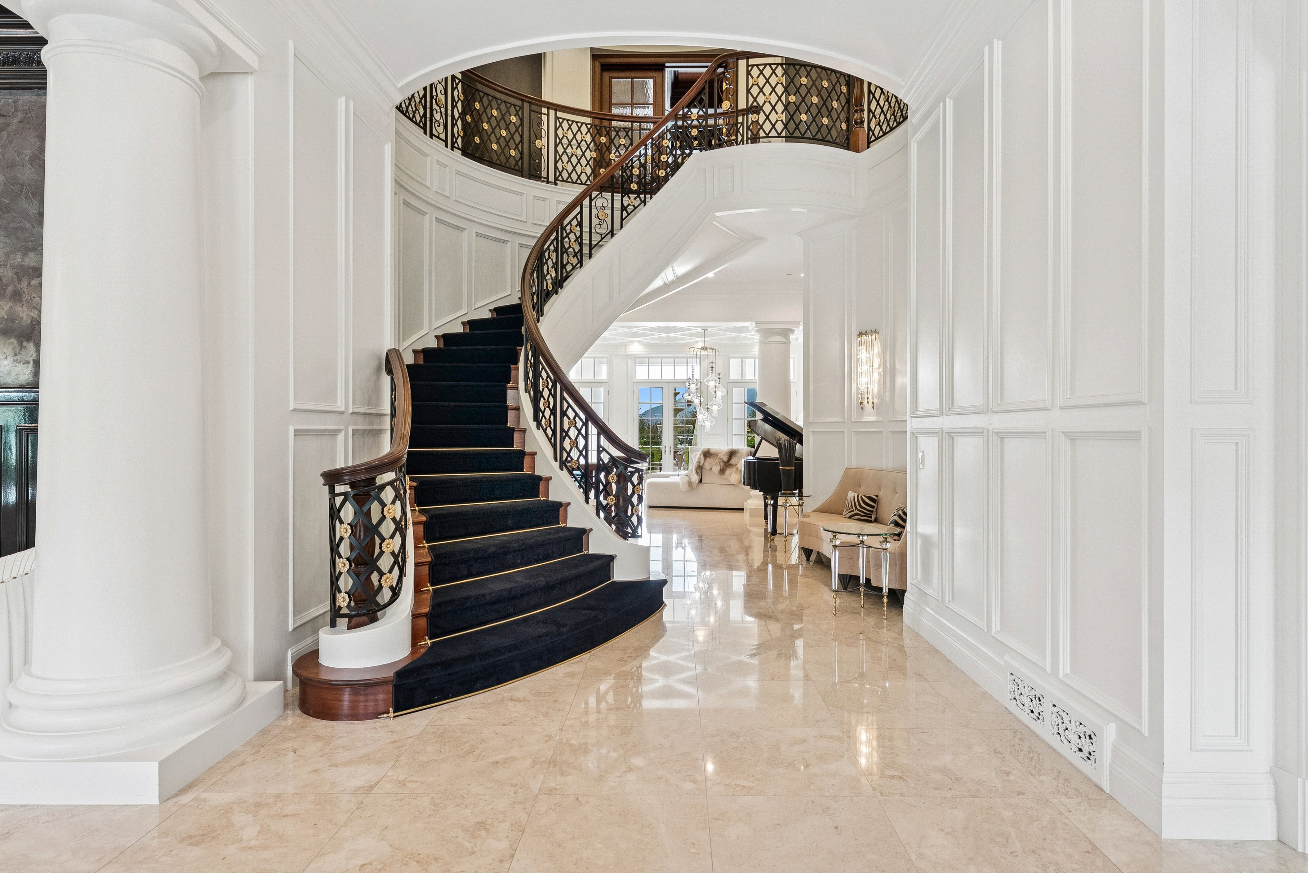 Grand entry featuring a curved staircase with dark wood handrails and ornate balusters, complemented by a black carpet runner