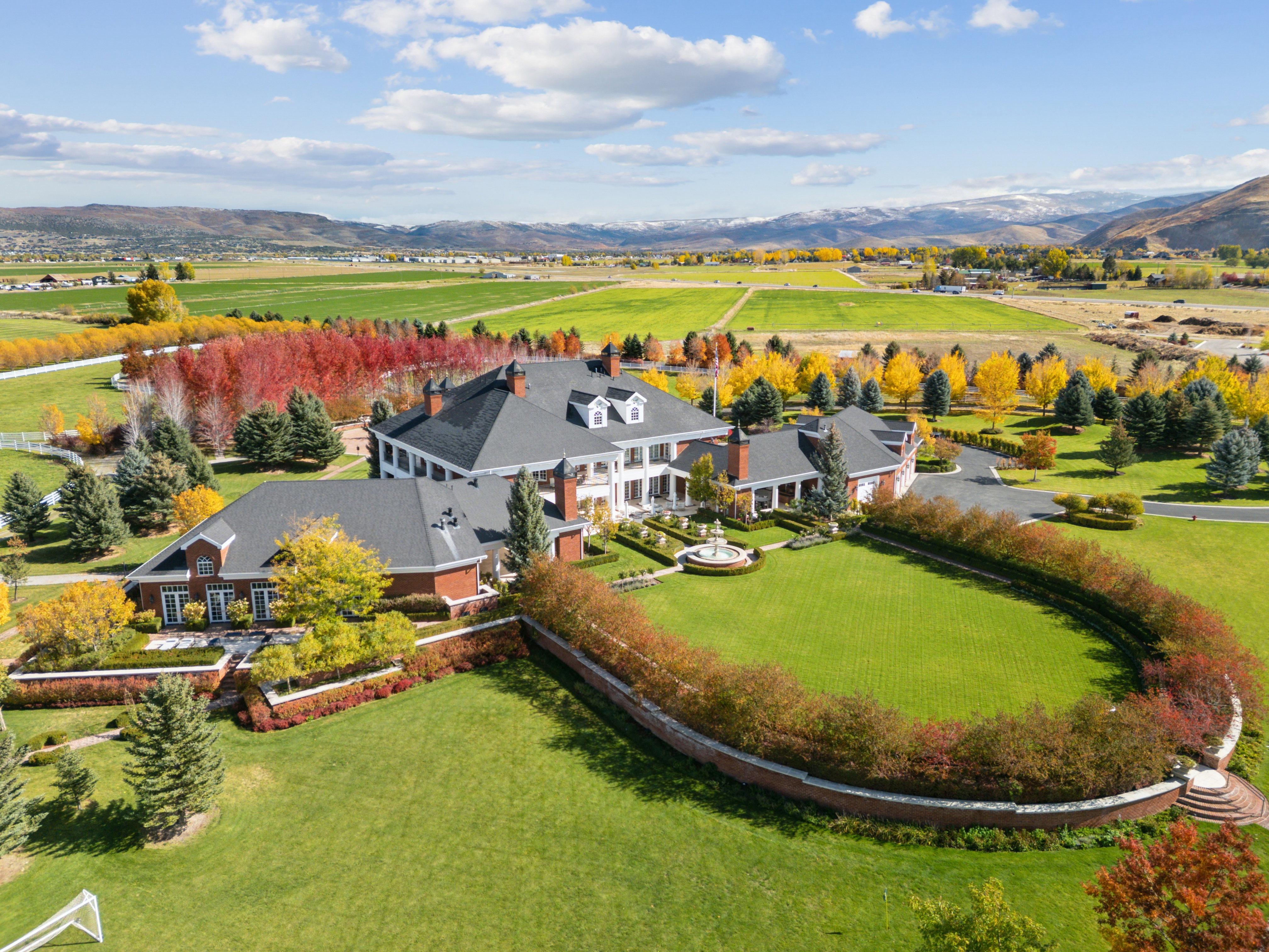 Expansive estate featuring a large main residence with brick and white column architecture, multiple gabled roofs, and dormer windows