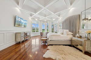 Bedroom with a chandelier, a decorative wall, coffered ceiling, beam ceiling, and wood finished floors