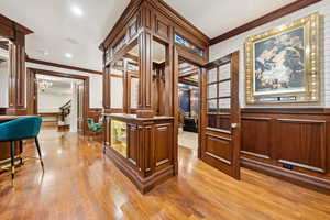 Corridor with crown molding, a chandelier, ornate columns, light wood finished floors, and wainscoting