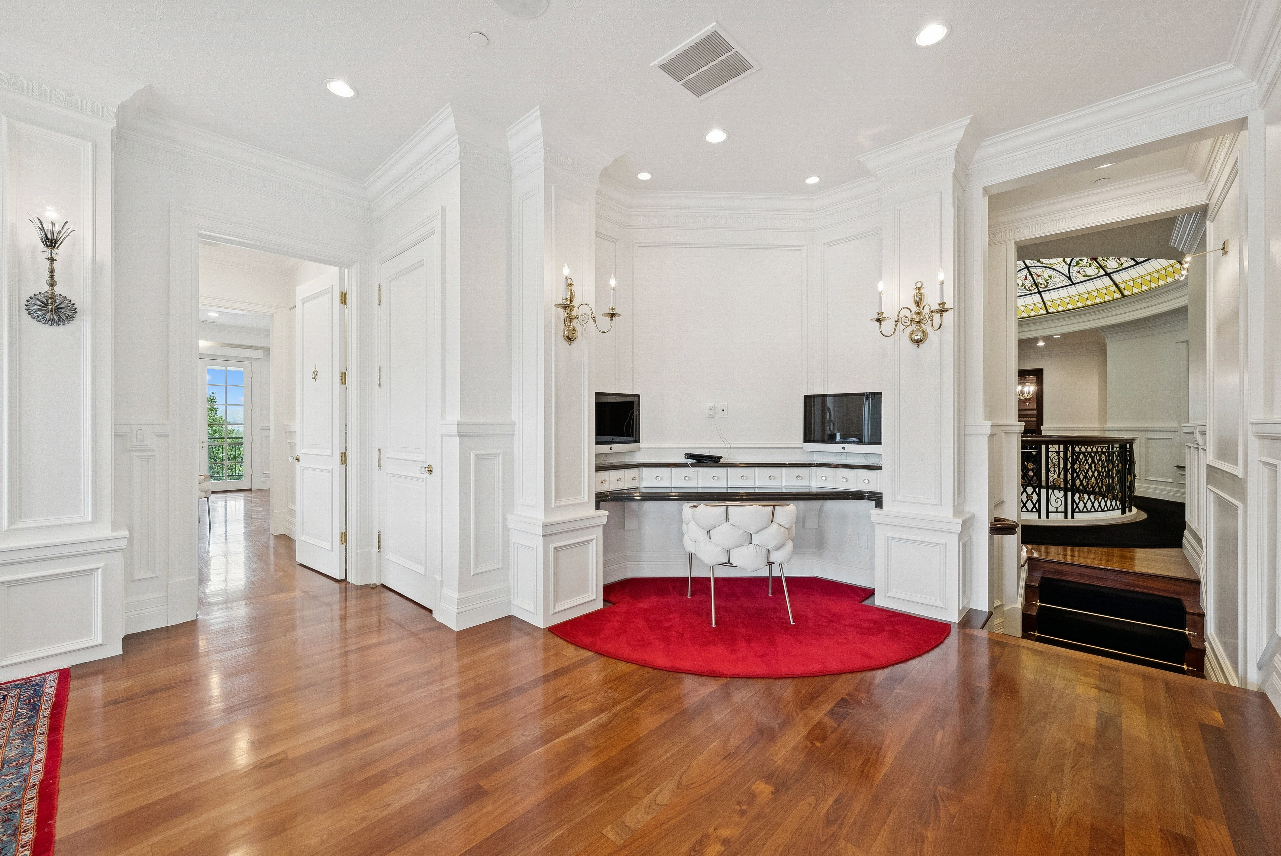 Hardwood flooring extending throughout, featuring intricate wall paneling and decorative sconces