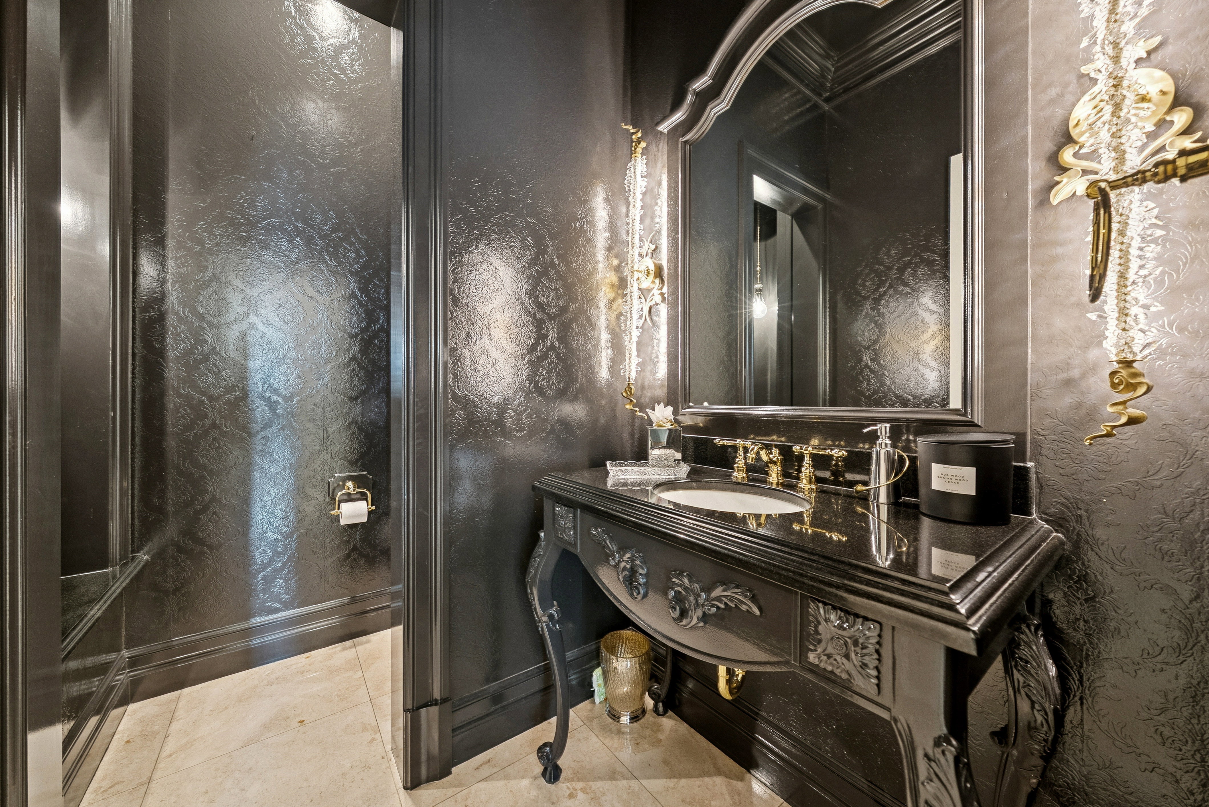Ornate vanity with carved detailing, a dark polished countertop, and gold-finish fixtures