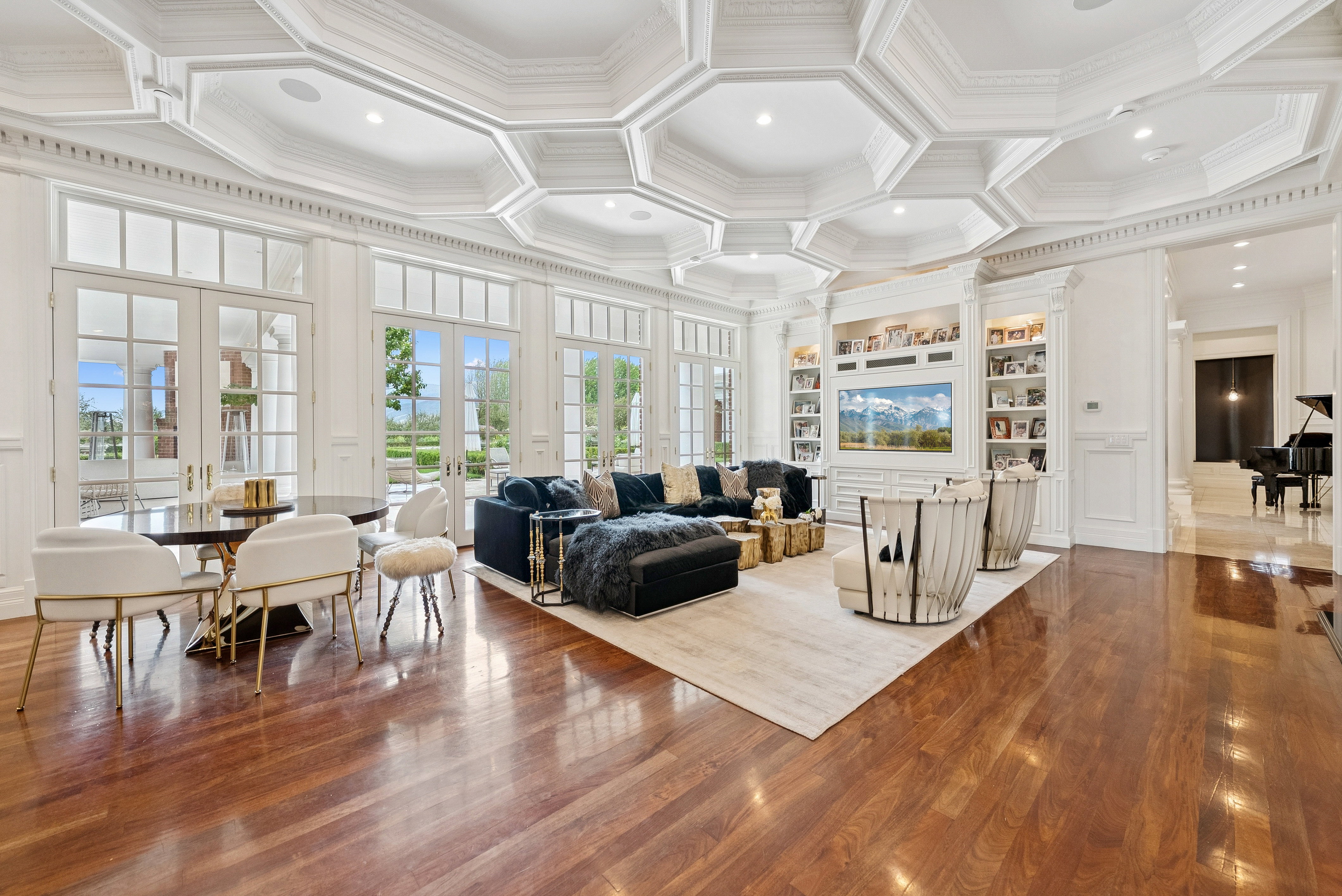 Expansive room featuring ornate coffered ceilings, rich wood-finish flooring, and multiple sets of French doors with transom windows