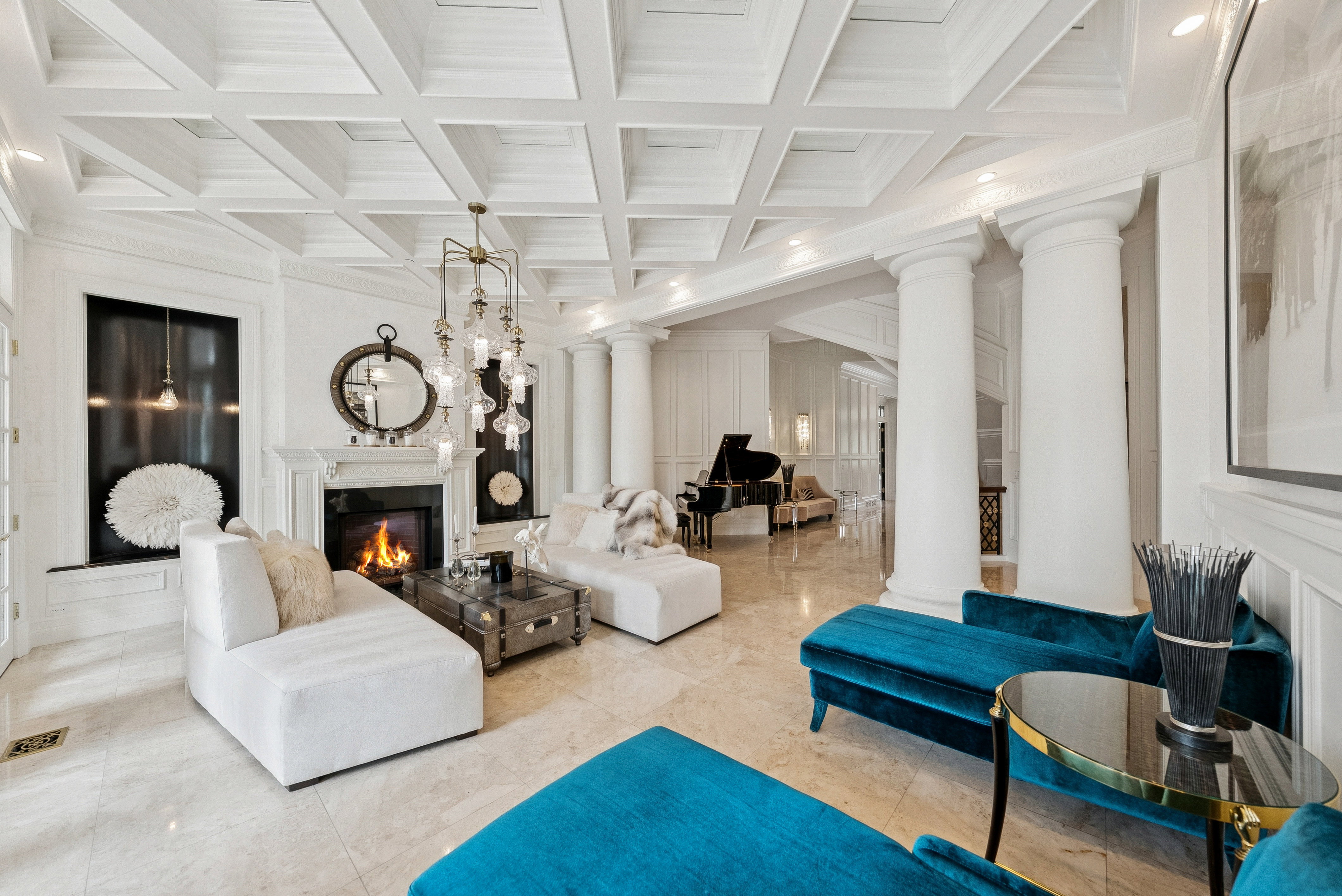 Spacious interior featuring a coffered ceiling, a fireplace with a white mantel, prominent architectural columns, polished stone flooring, and recessed lighting