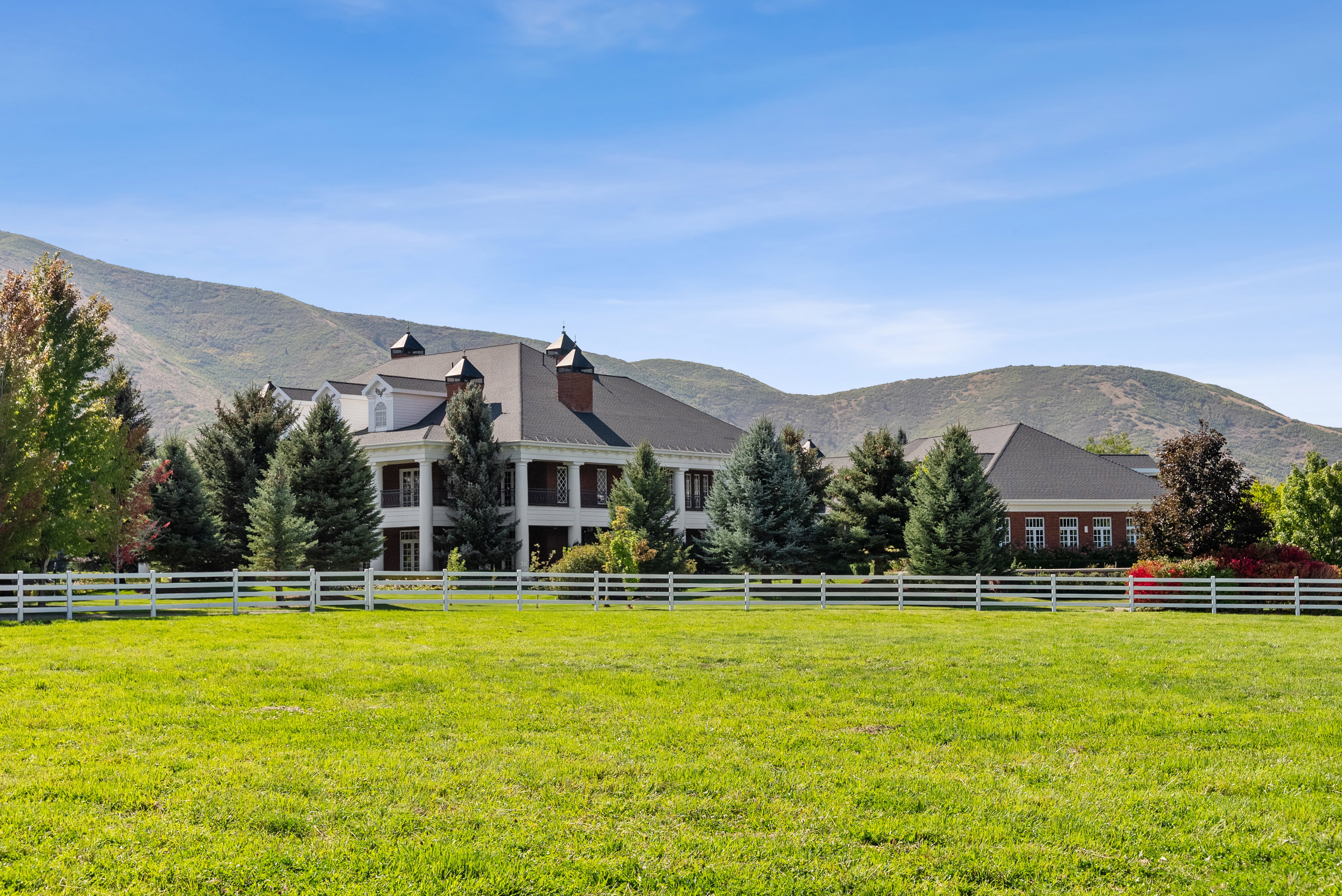 Expansive green field featuring a white fence and mature trees