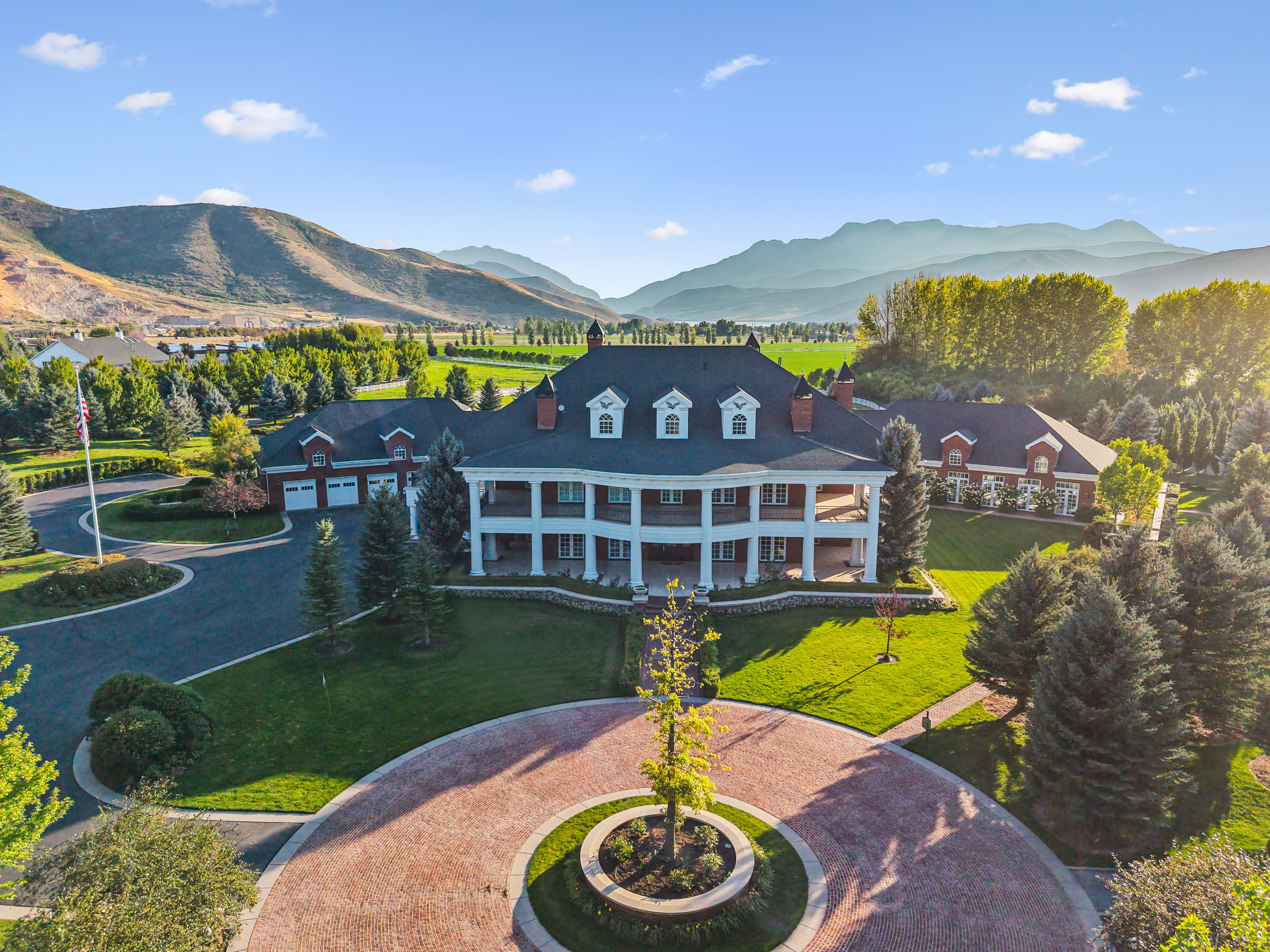 Grand estate featuring a red brick facade with white columns, a multi-car garage, and a circular paver driveway