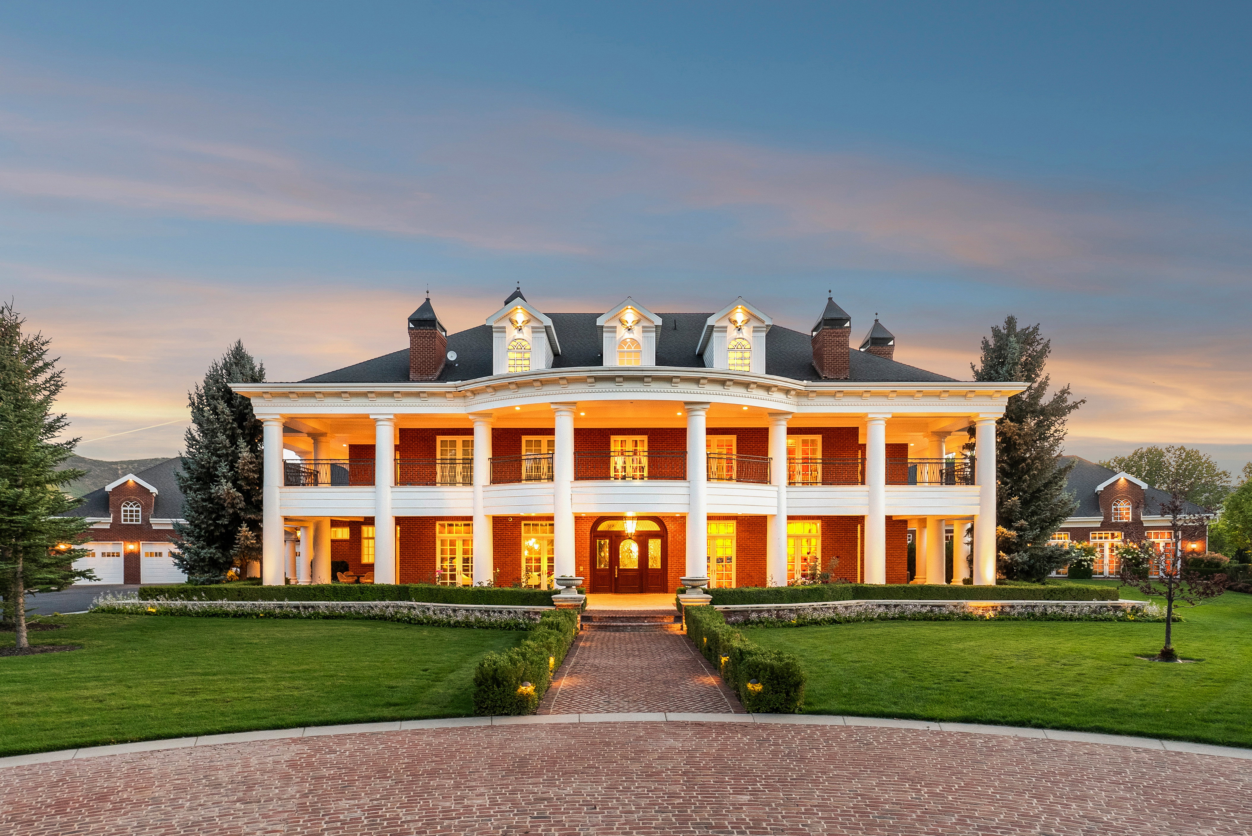 Stately brick residence featuring a two-story portico with white columns, multiple dormer windows, and a classic black shingle roof