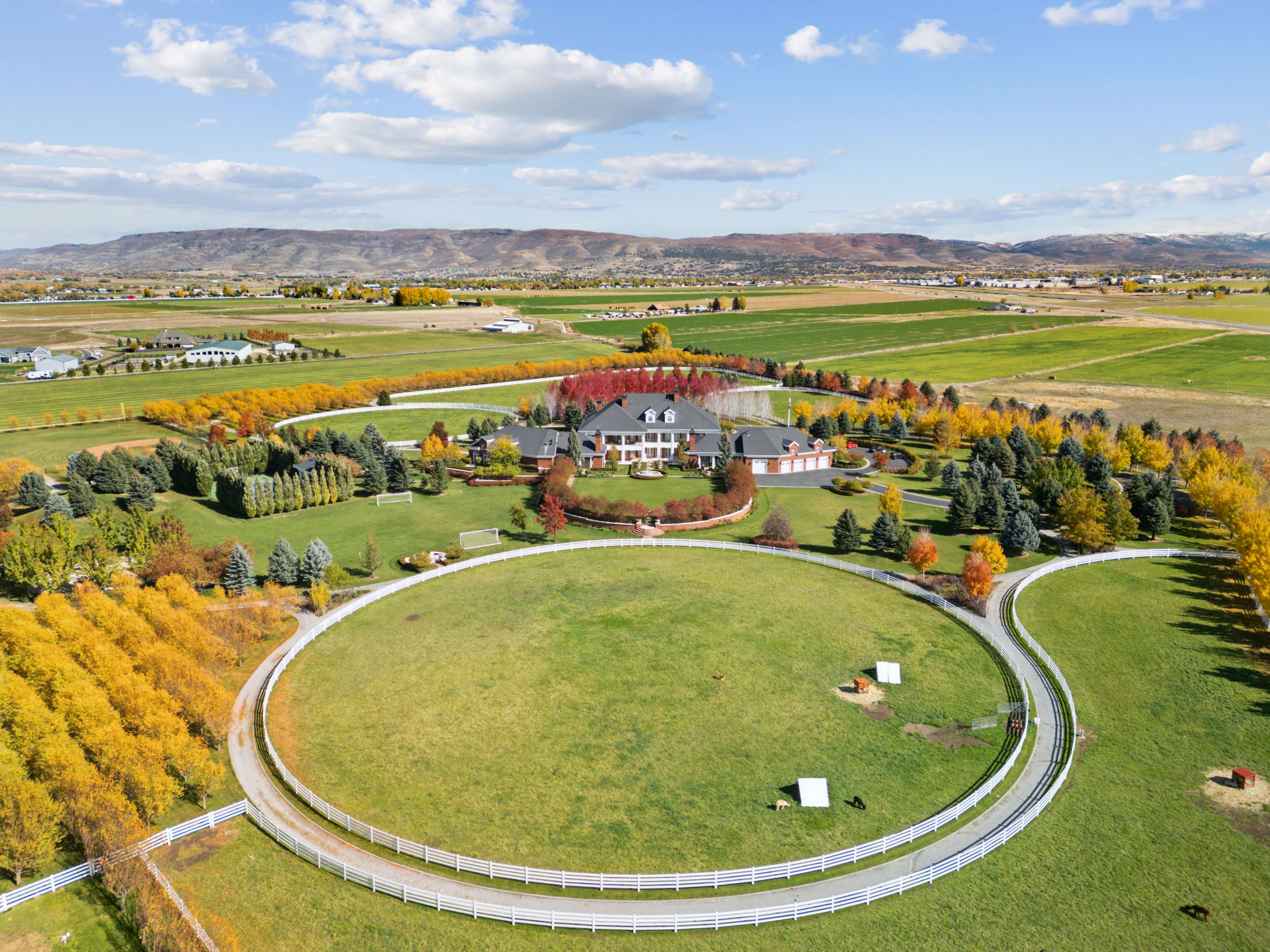 Expansive property featuring a grand estate, circular driveways, mature trees with autumn foliage, and a mountain backdrop