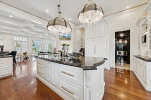 Kitchen featuring white cabinets, ornamental molding, decorative light fixtures, a center island, and dark stone counters