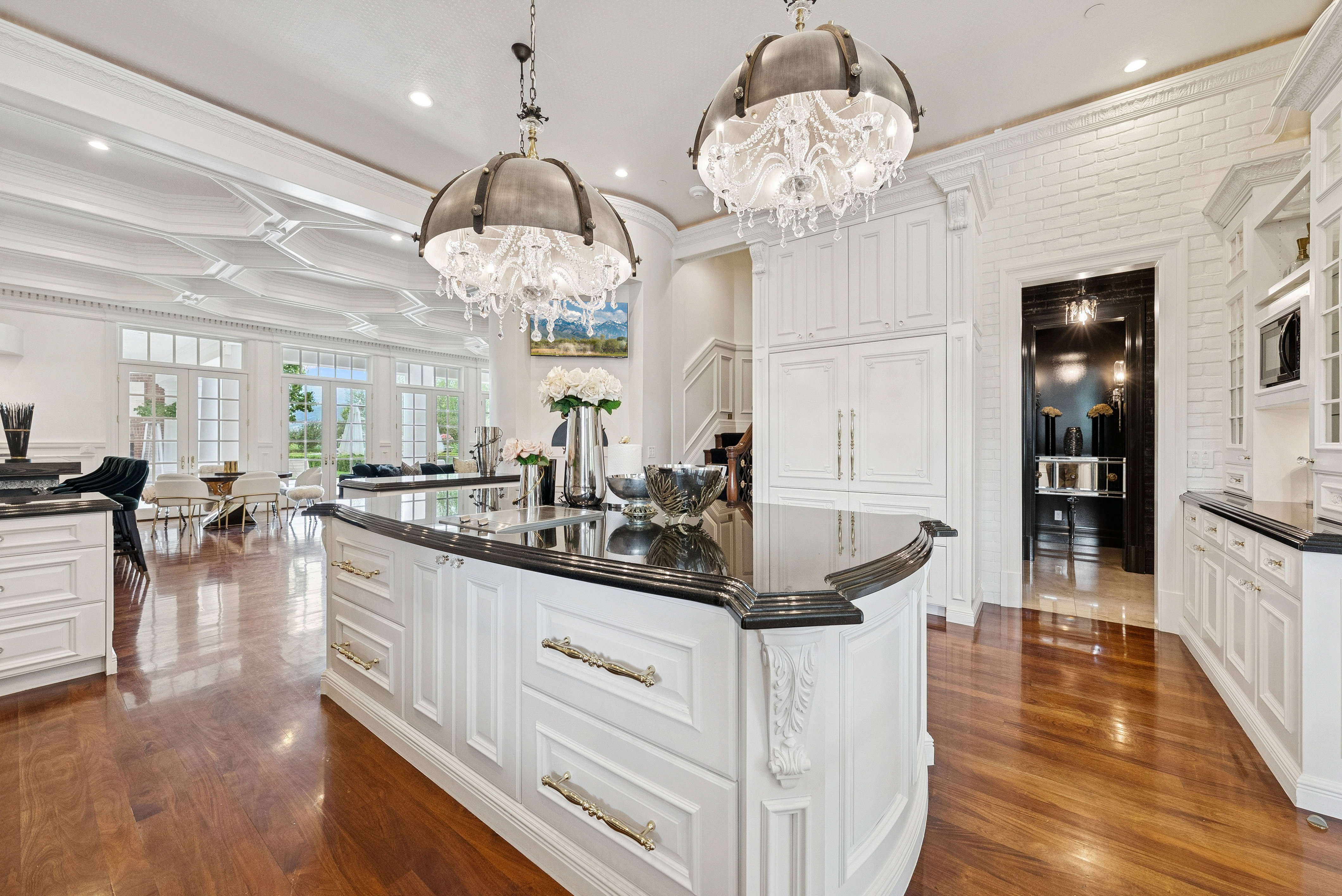 Gourmet kitchen featuring a large island with dark stone countertops, custom white cabinetry, and two ornate chandeliers