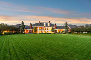 Back of property at dusk with a chimney and a lawn