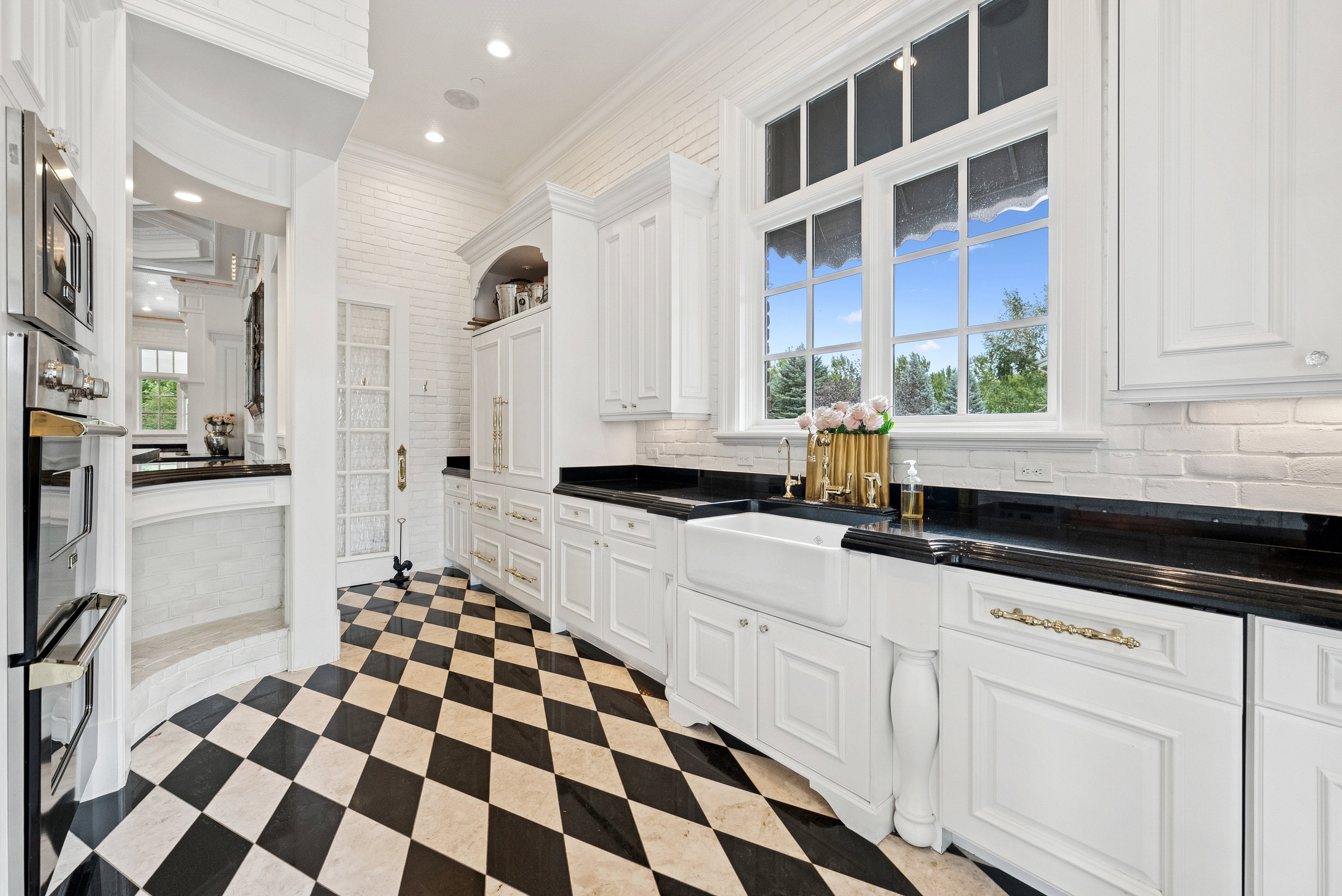 Kitchen featuring black and white checkerboard flooring, white cabinetry with black countertops, a farmhouse sink, and stainless steel built-in appliances