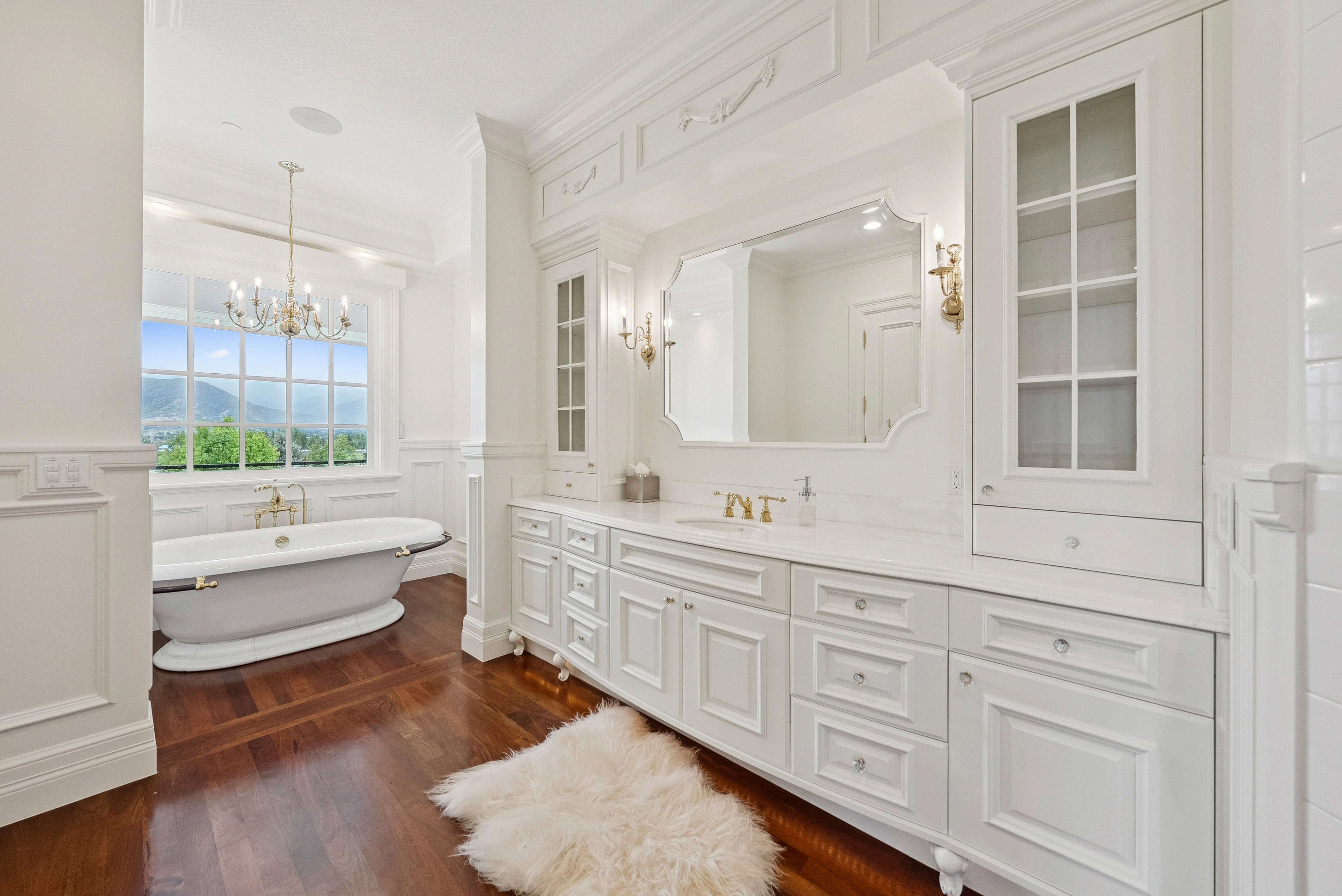 White freestanding soaking tub with brass fixtures and a grid-pattern window