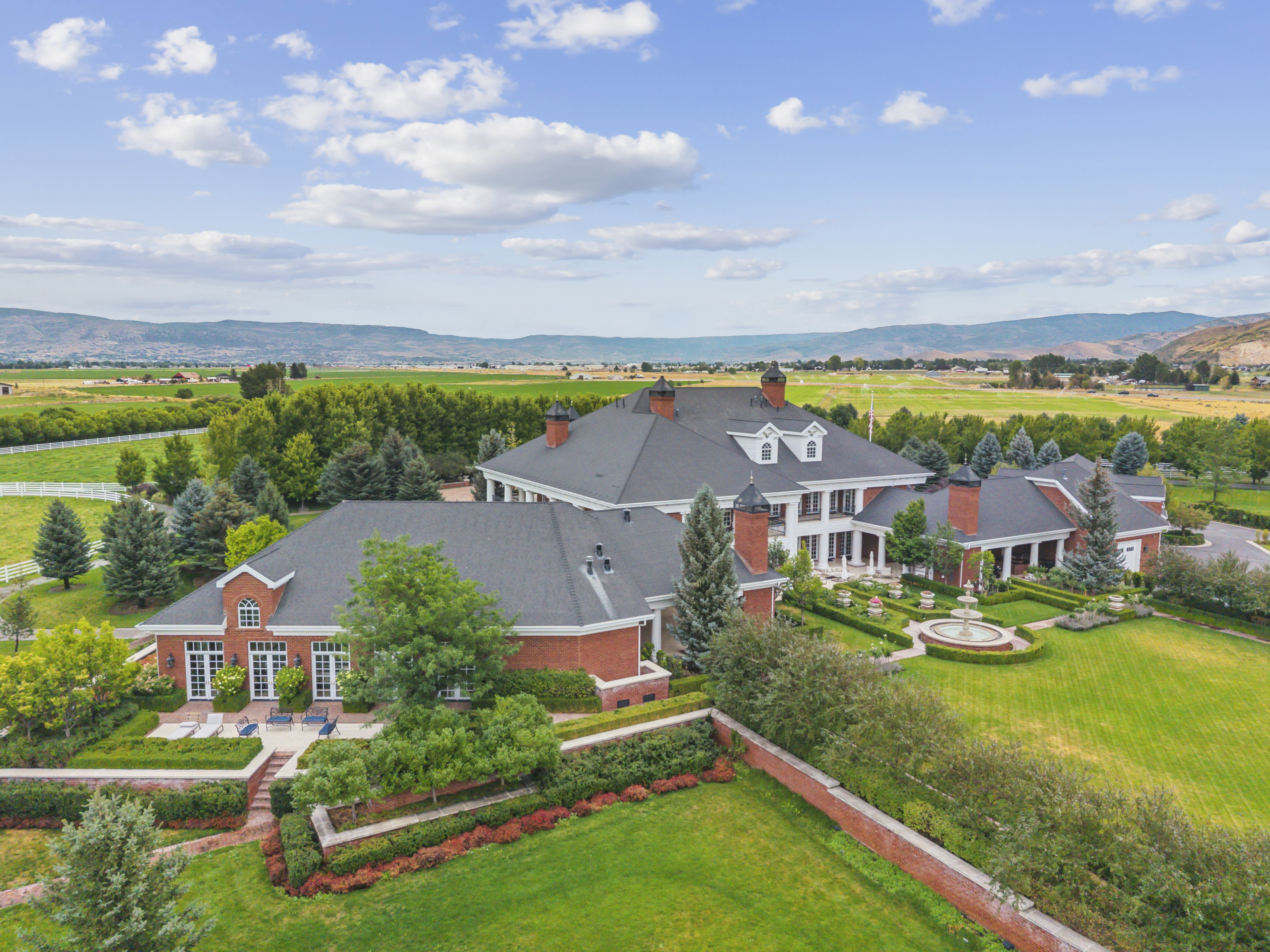 Expansive estate featuring a red brick exterior, multiple dormer windows, and a dark shingle roof