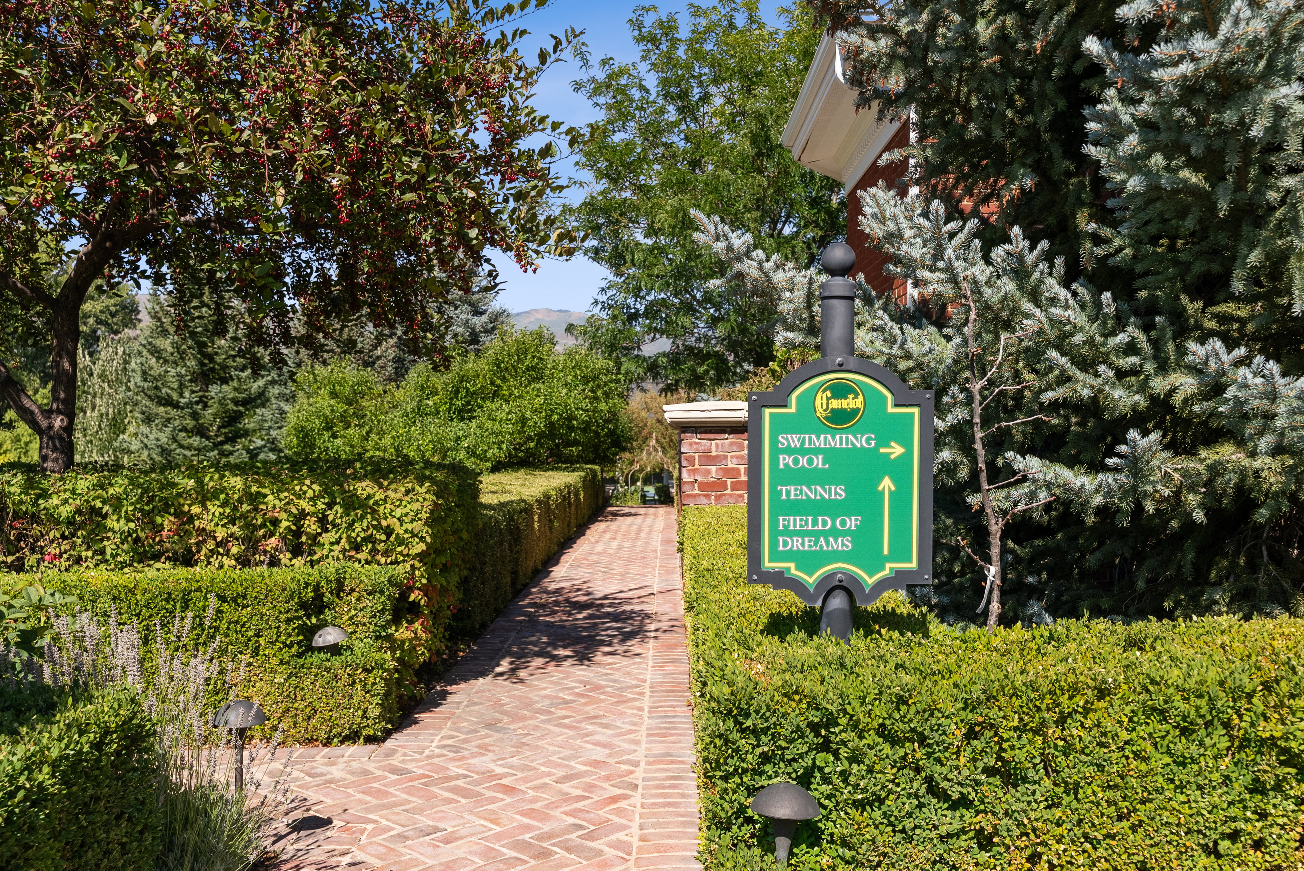 Brick paver pathway bordered by manicured hedges and mature trees