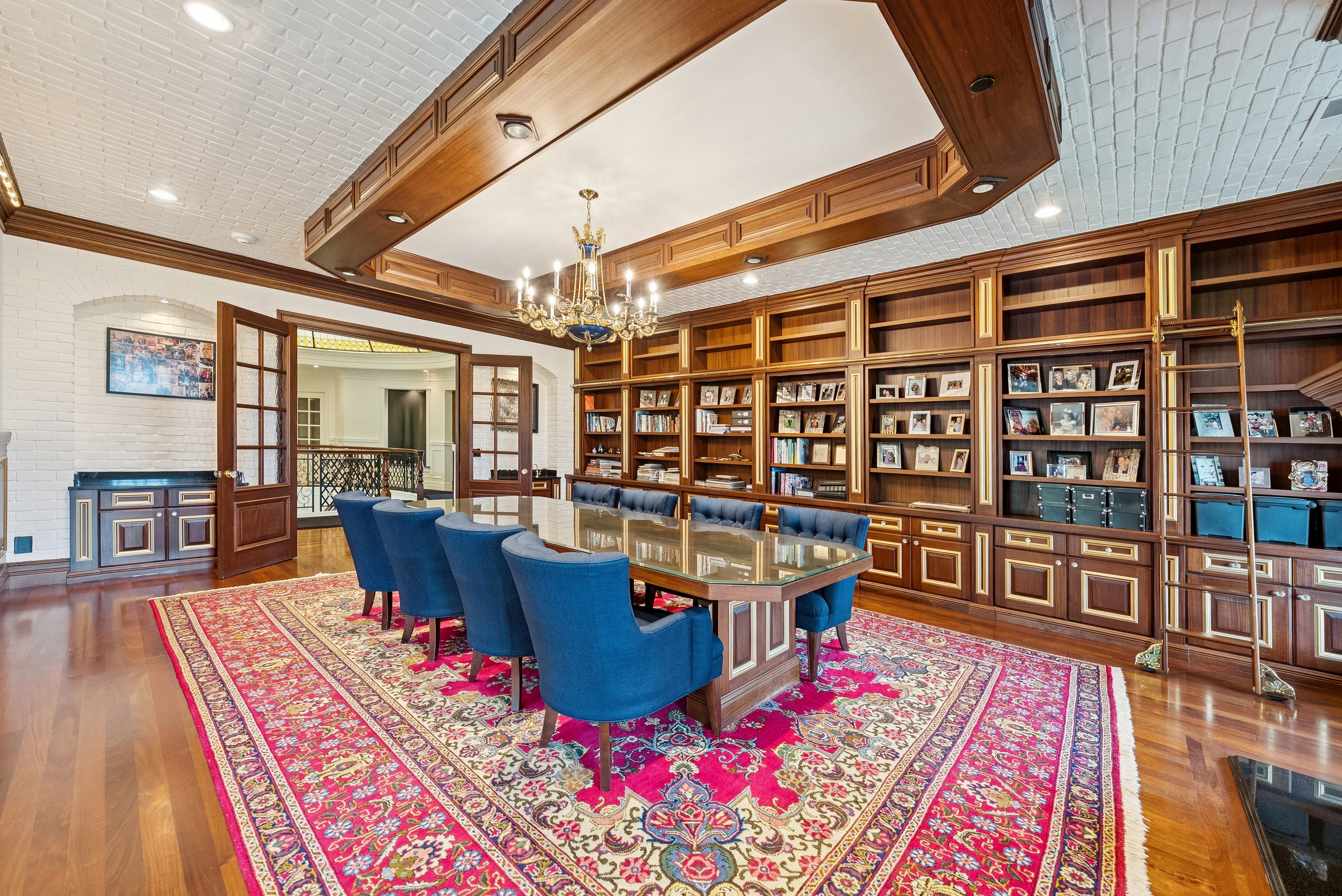 Expansive room featuring hardwood flooring, extensive built-in shelving with integrated cabinetry, a white brick-patterned ceiling, and a prominent chandelier