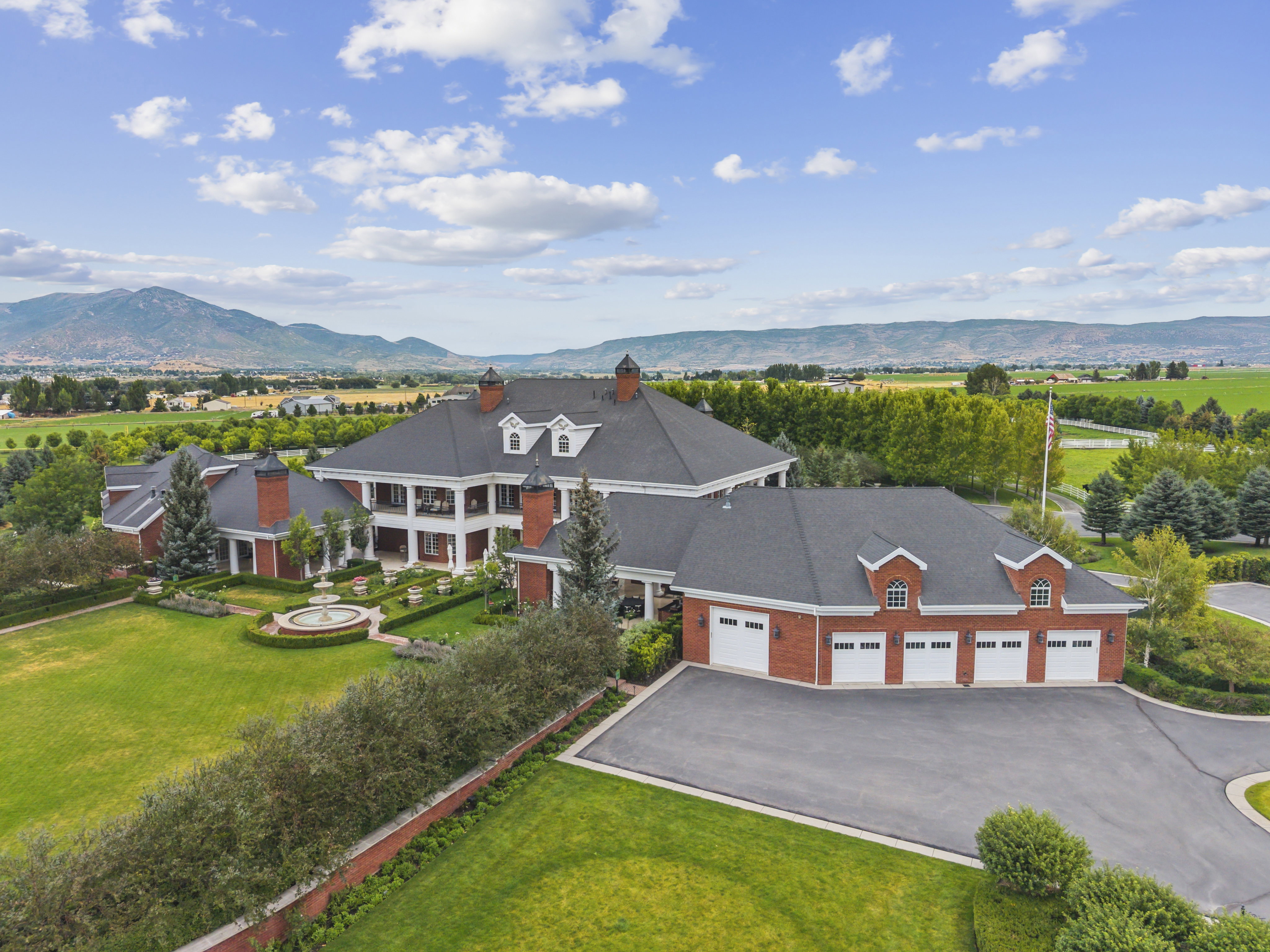 Sprawling brick estate featuring a multi-car garage, extensive green lawns, and a central tiered fountain