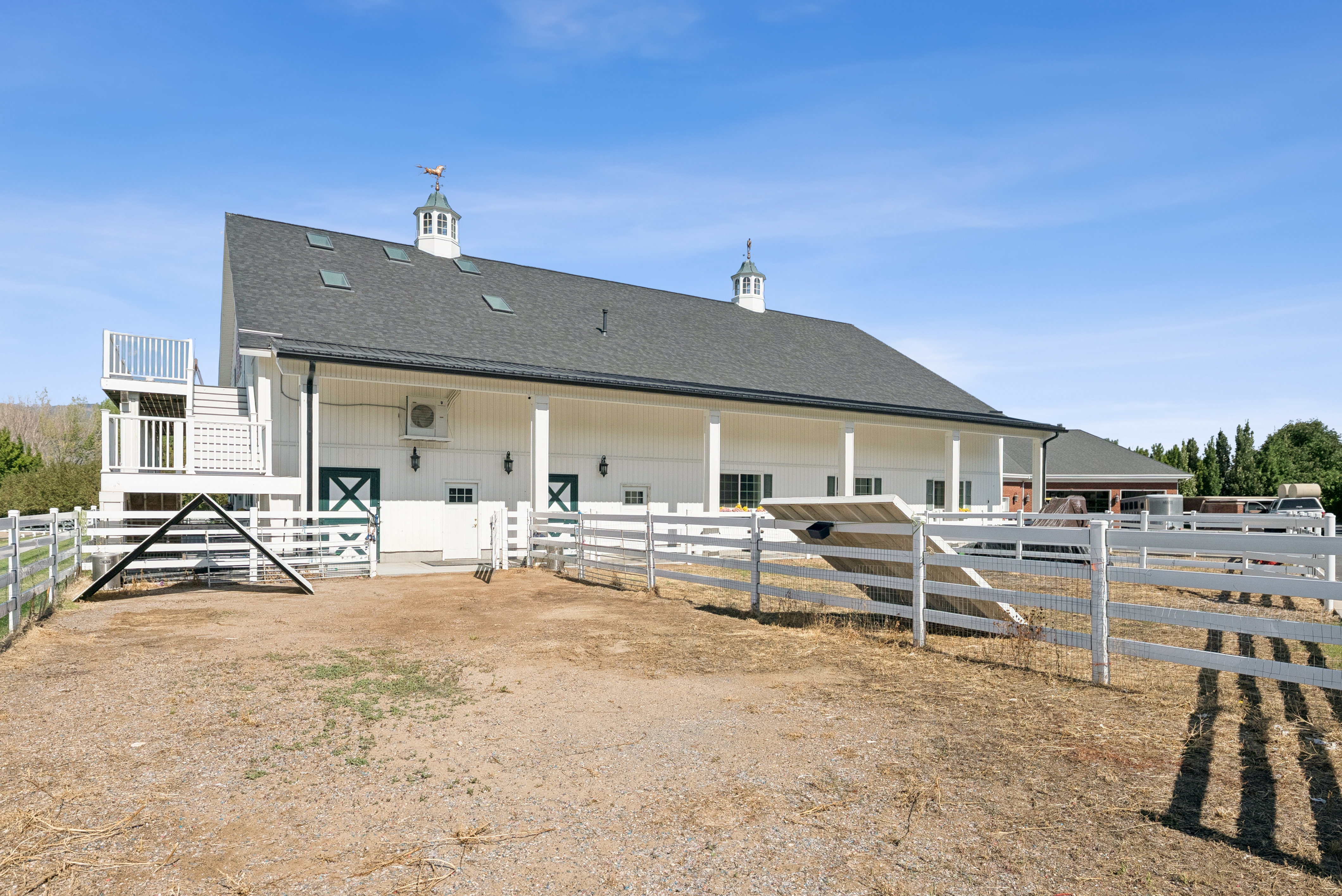 White barn-style structure featuring a dark gray shingle roof, multiple skylights, and a cupola with a weathervane