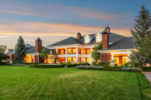 Back of property at dusk with a yard, brick siding, a chimney, and a balcony
