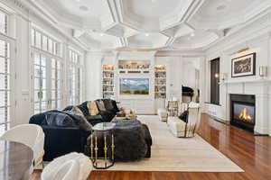 Living area featuring wood finished floors, beam ceiling, crown molding, a fireplace with flush hearth, and coffered ceiling