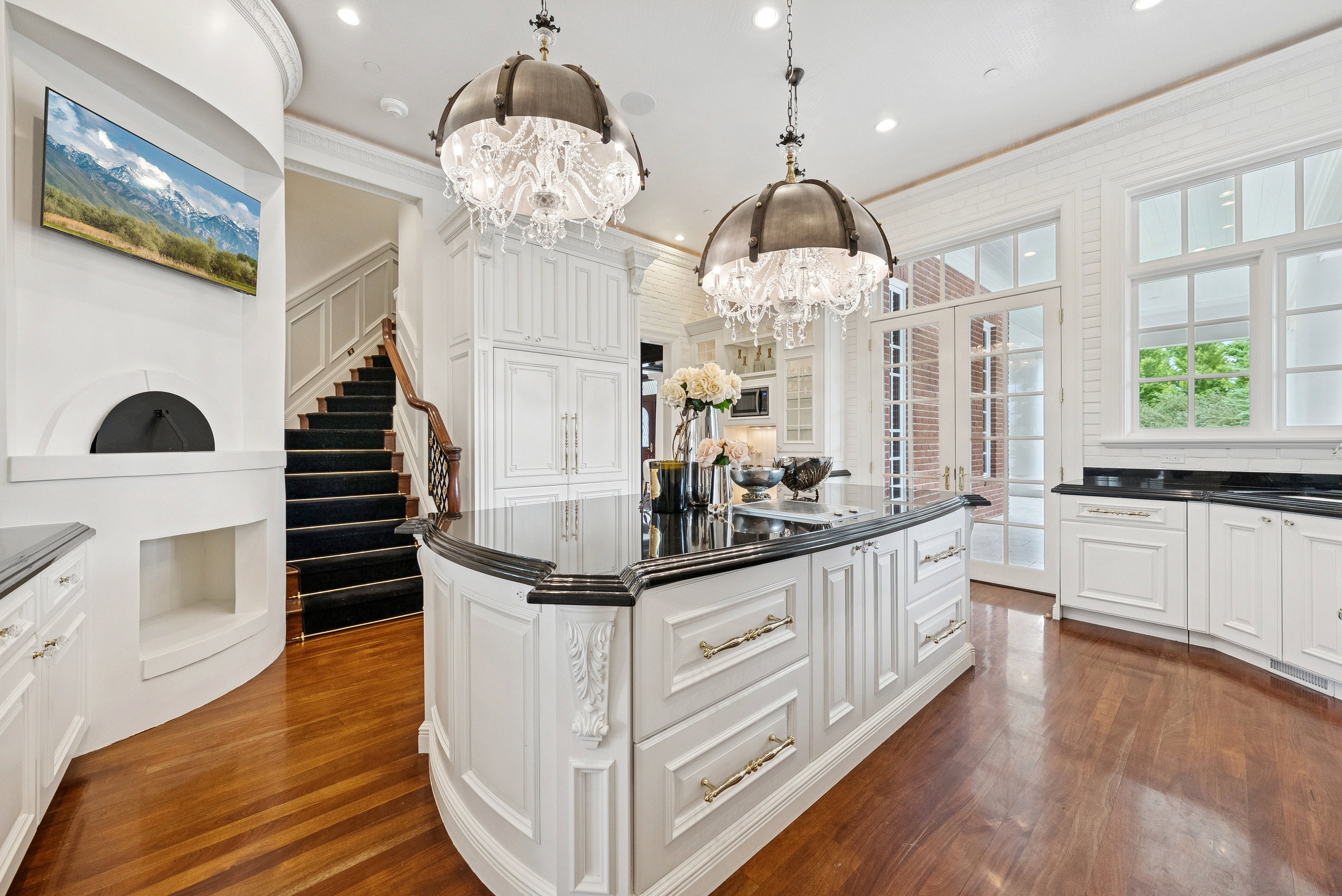 Gourmet kitchen with a large island featuring a black countertop, white cabinetry with ornate detailing, and two chandelier light fixtures