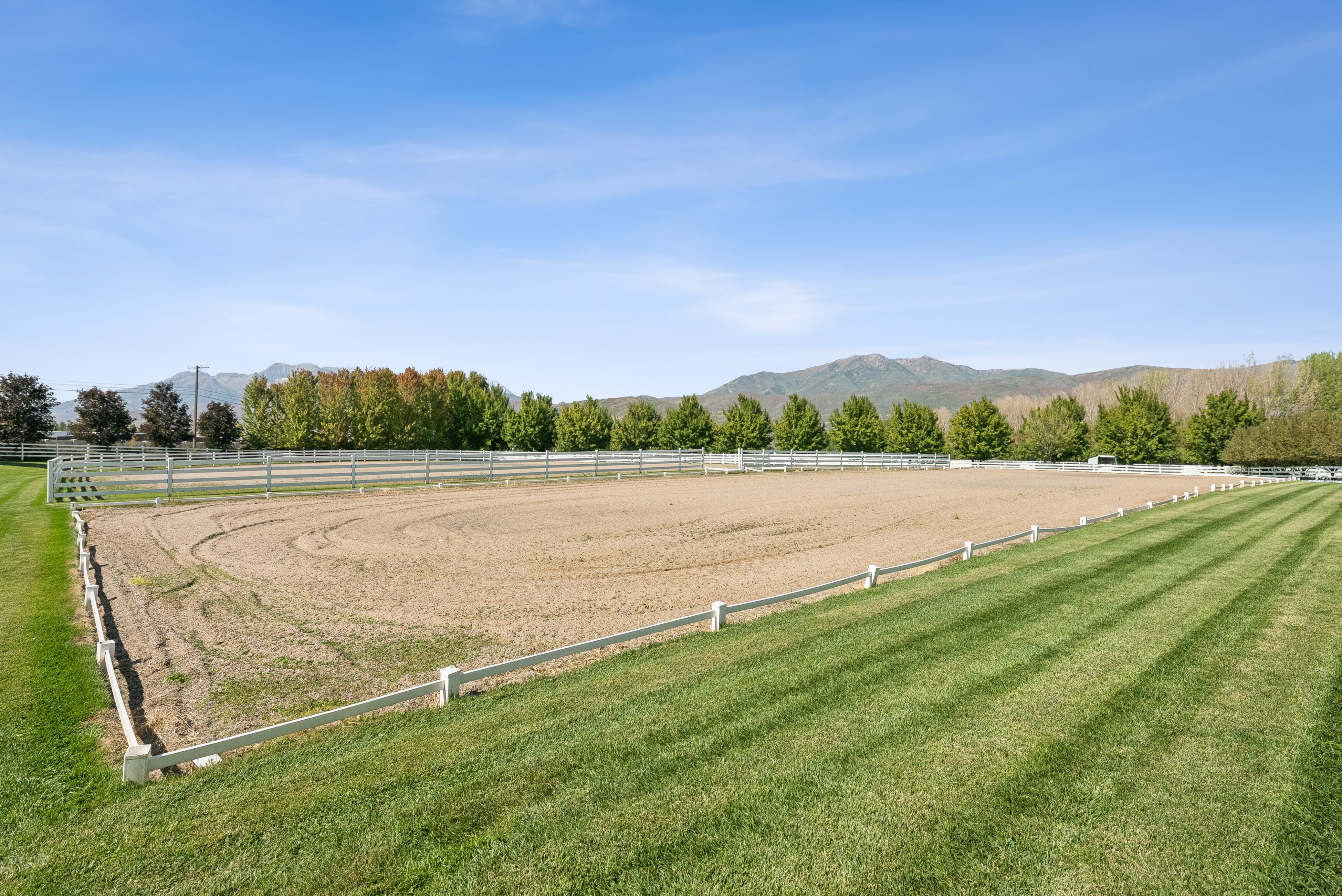 Expansive outdoor riding arena with a sand surface, bordered by white fencing