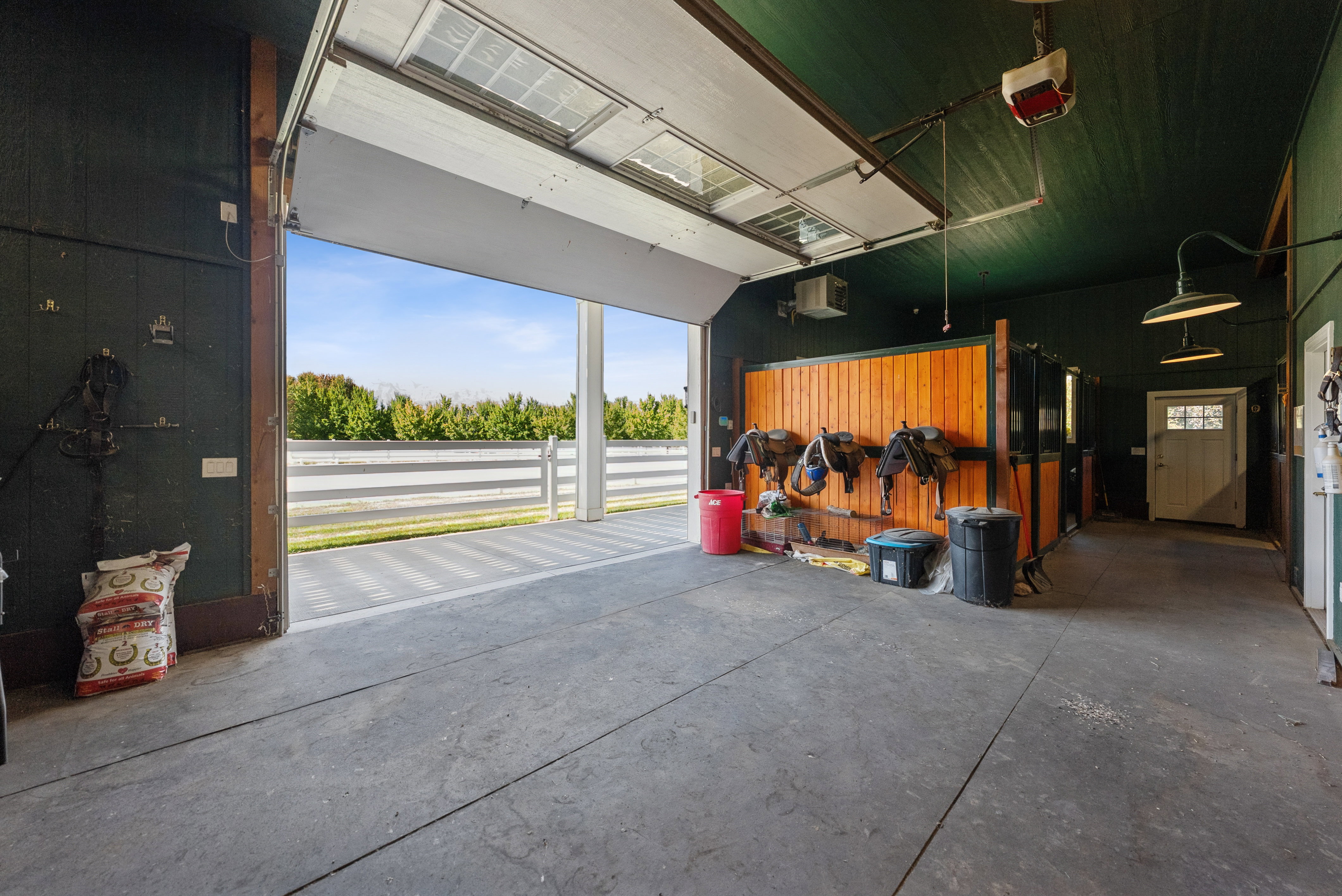 Spacious interior barn area featuring a large overhead door, concrete flooring, rich wood-paneled walls, and built-in lighting fixtures