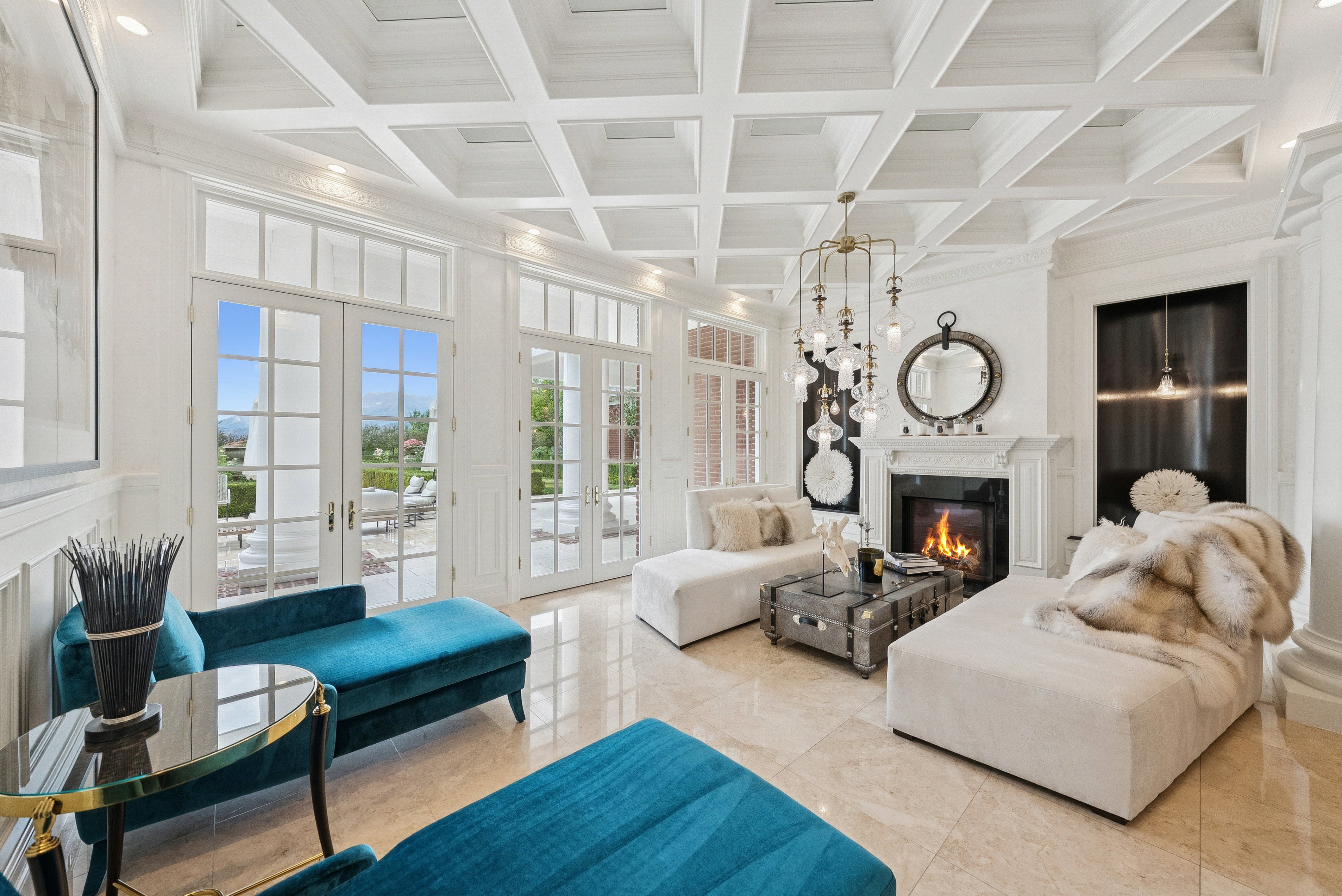 Spacious living area featuring a coffered ceiling, multiple sets of French doors, an ornate fireplace with a mantel, polished tile flooring, and a decorative chandelier
