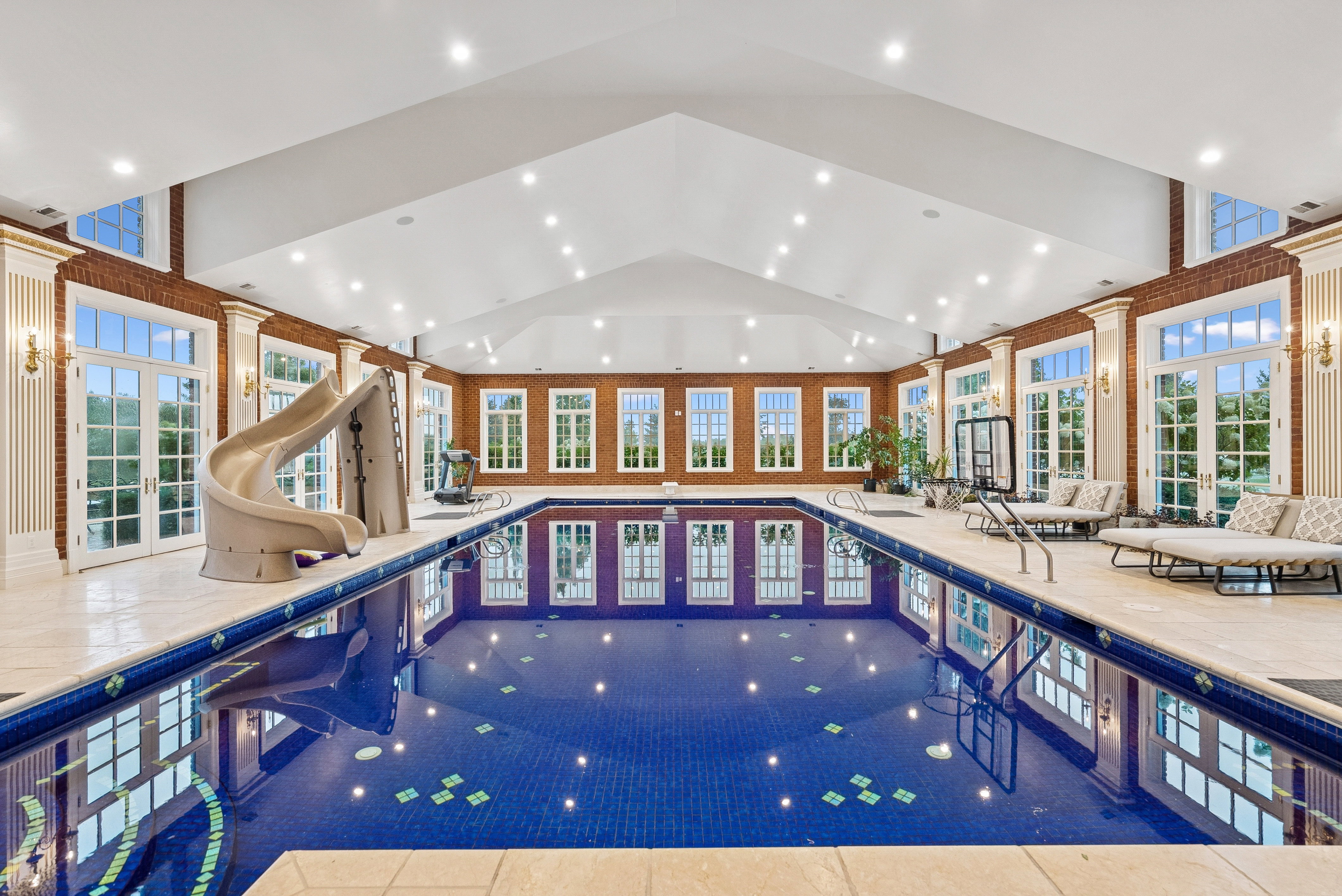 Indoor swimming pool featuring blue mosaic tile, a pool slide, and multiple French doors