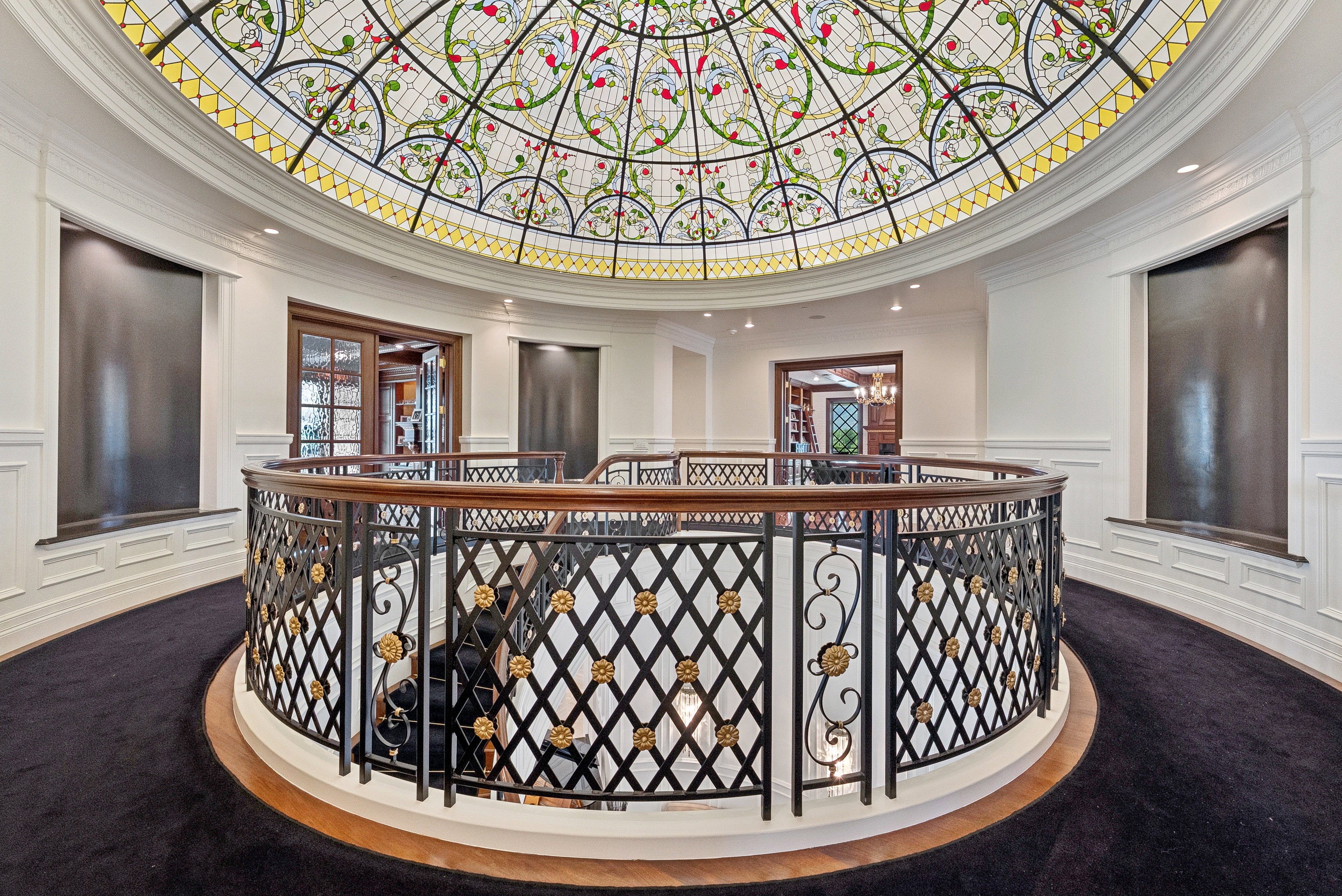 Grand foyer featuring a domed stained-glass ceiling, ornate wrought iron and wood-finish railing, dark carpeting, and built-in wall fountains